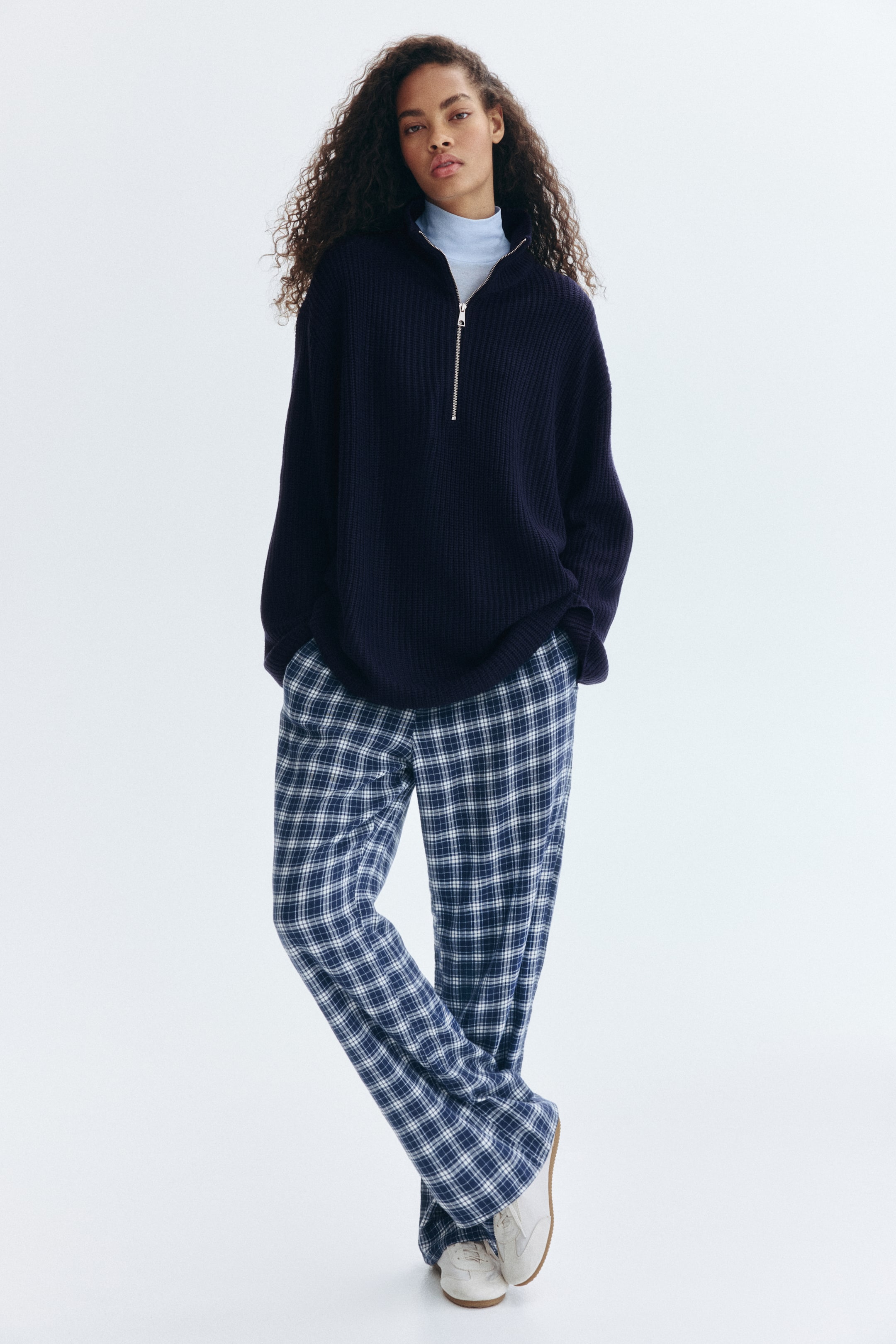 View larger image: A navy blue ribbed half-zip sweater is being worn by the model, layered over a light blue turtleneck. Blue and white plaid relaxed-fit pants are also being worn, with the model's hands placed in the pockets.