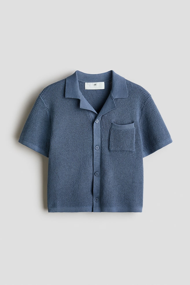 A blue short-sleeved knitted shirt is shown from the front. It features a spread collar, a full button-front fastening with matching buttons, and a single patch pocket on the left chest, highlighting a textured waffle knit. - 1