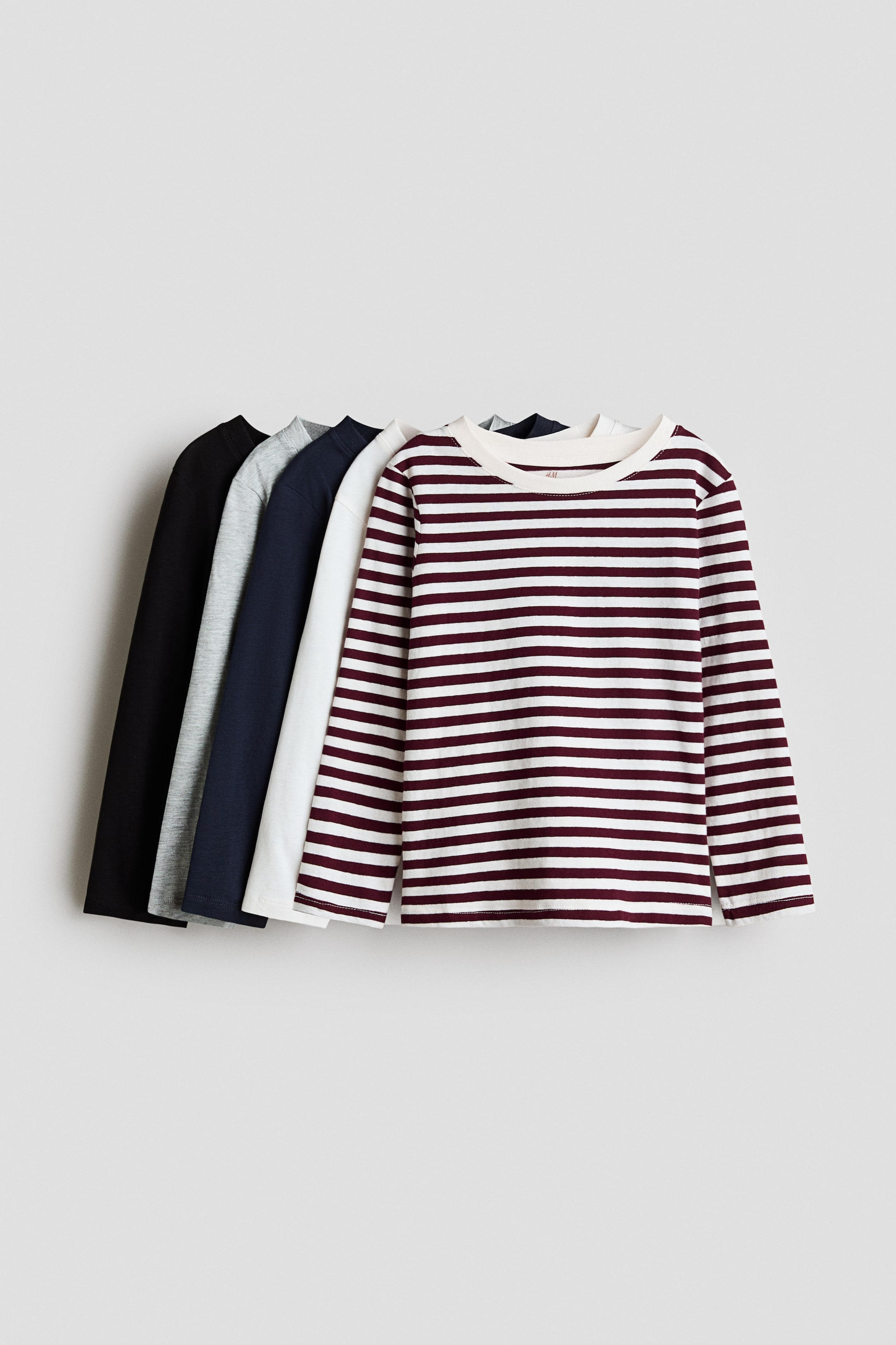 View larger image: Five long-sleeve cotton jersey tops are layered and facing front, showcasing a burgundy and white horizontally striped top at the forefront. The remaining solid-coloured tops layered behind are in white, navy blue, heather grey, and black, all featuring a round neckline with a narrow trim.