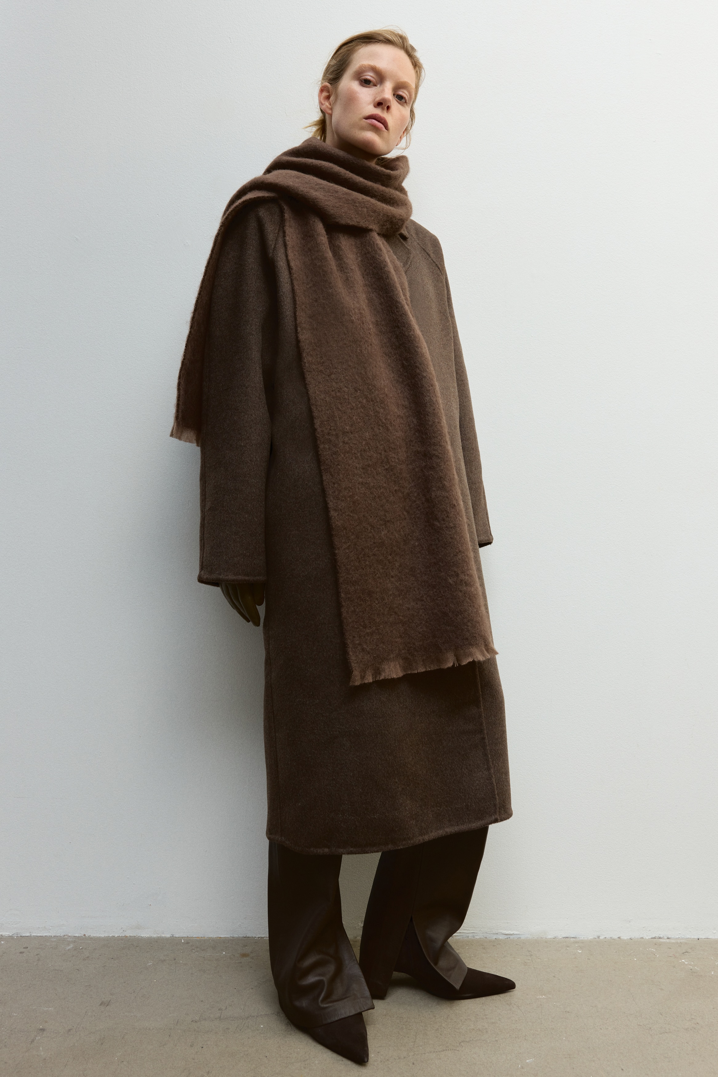 A dark brown scarf featuring a soft, brushed texture is laid folded flat in a front-facing view, showcasing short, delicate fringed edges at the bottom.