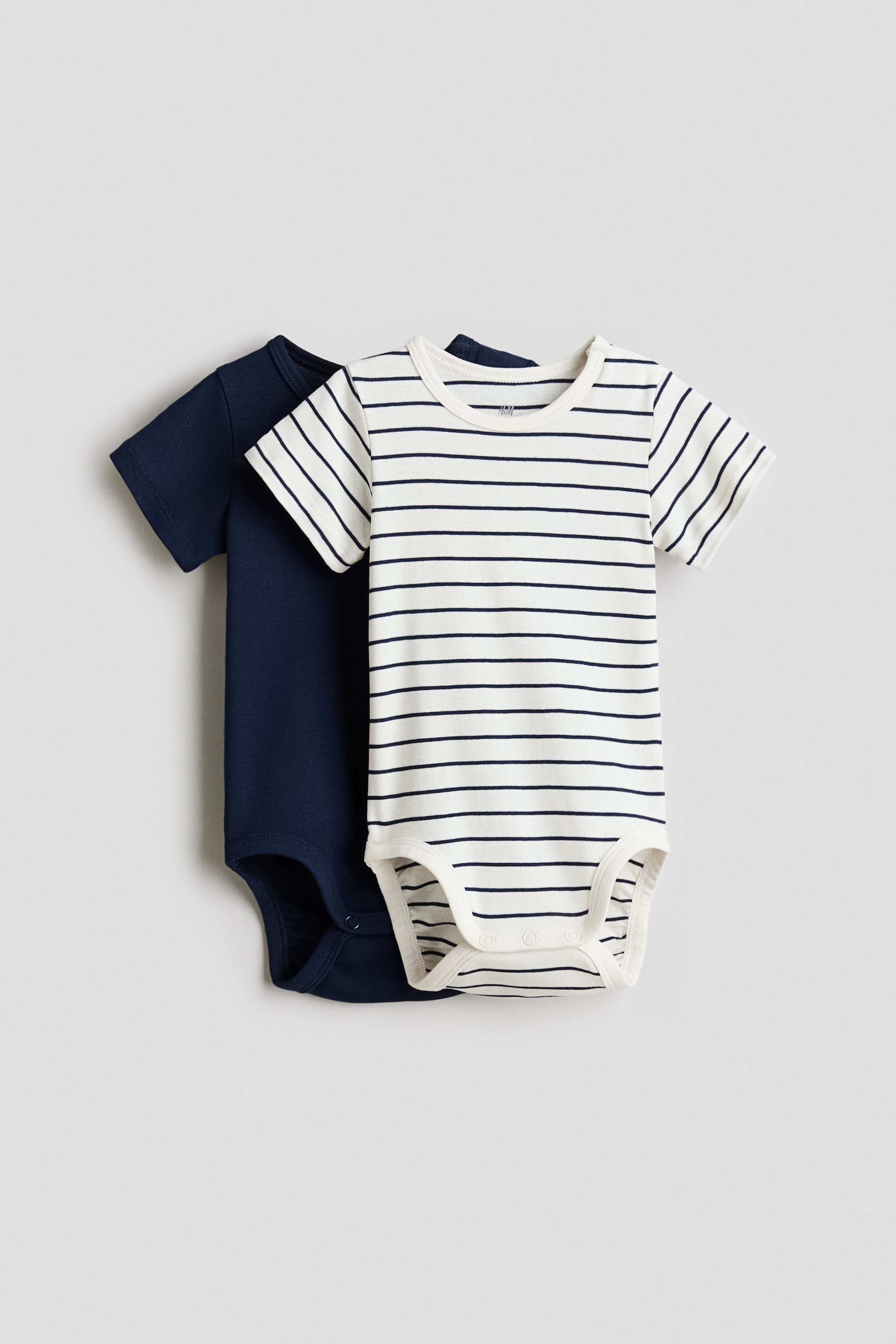 Vis større bilde: To babybodyer vises, en ensfarget marineblå og en off-white med marineblå horisontale striper. Den stripete bodyen overlapper delvis den marineblå, og begge har korte ermer, rund hals og trykknapper i skrittet.