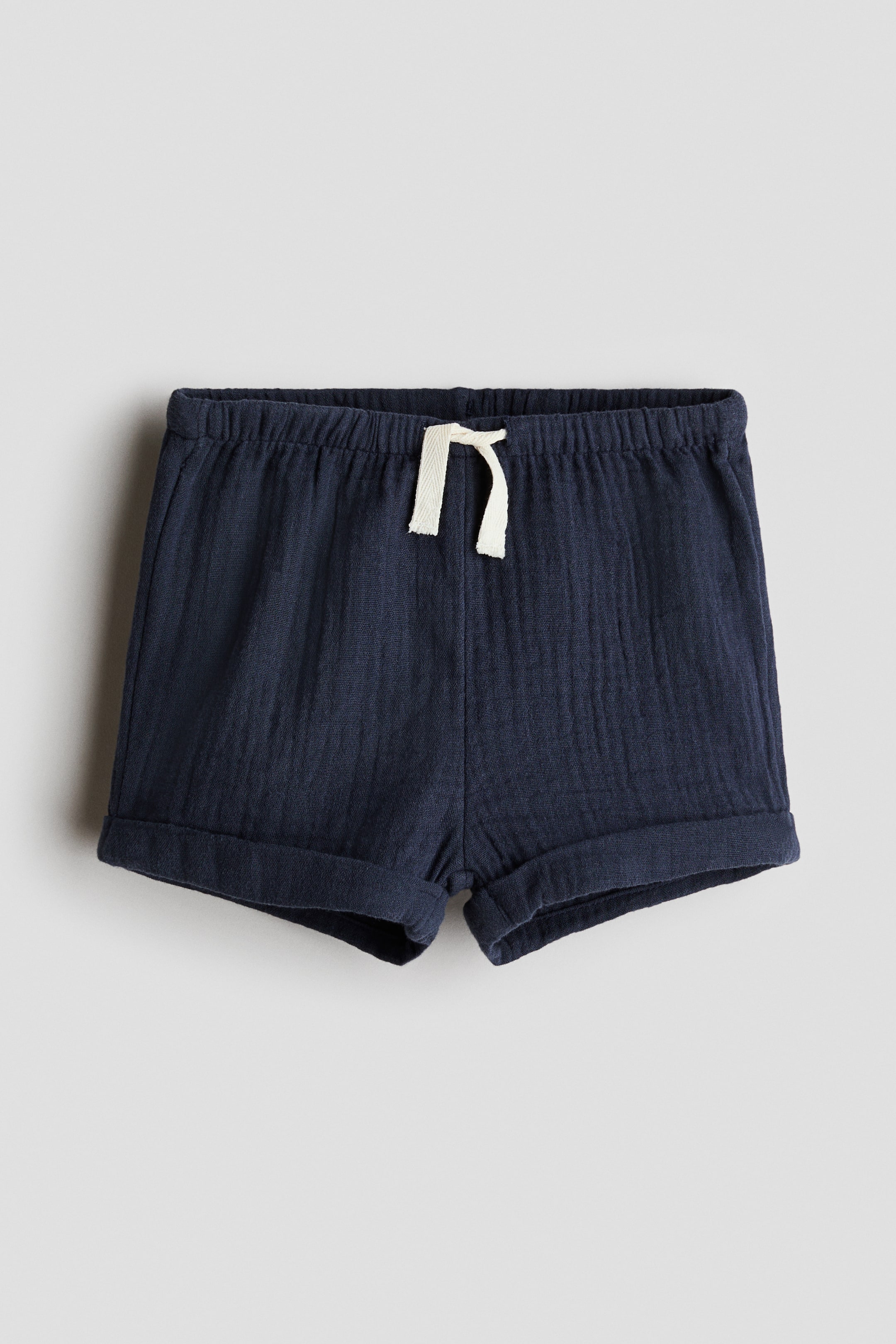 Agrandir l'image: Les shorts en mousseline bleu marine sont présentés de face, avec une taille élastiquée ornée d'un cordon clair noué en nœud, et des revers cousus aux ourlets.