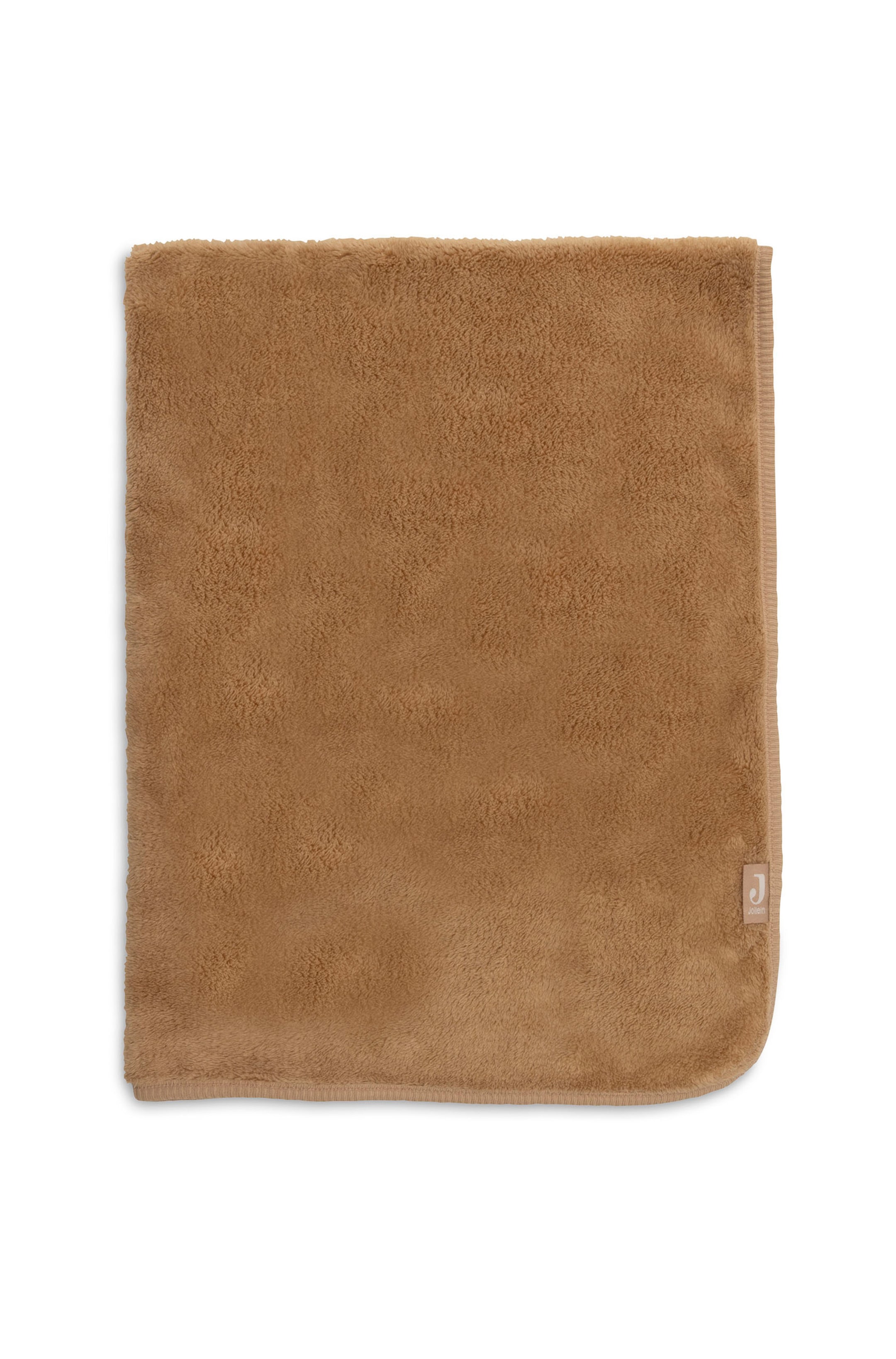 Agrandir l'image: Une couverture en polaire peluche camel marron est posée à plat, mettant en valeur sa surface douce et texturée ainsi que ses bords ourlés. La couverture présente un coin inférieur droit arrondi avec une petite étiquette en tissu beige clair affichant une lettre « J » blanche, cousue près de la bordure.