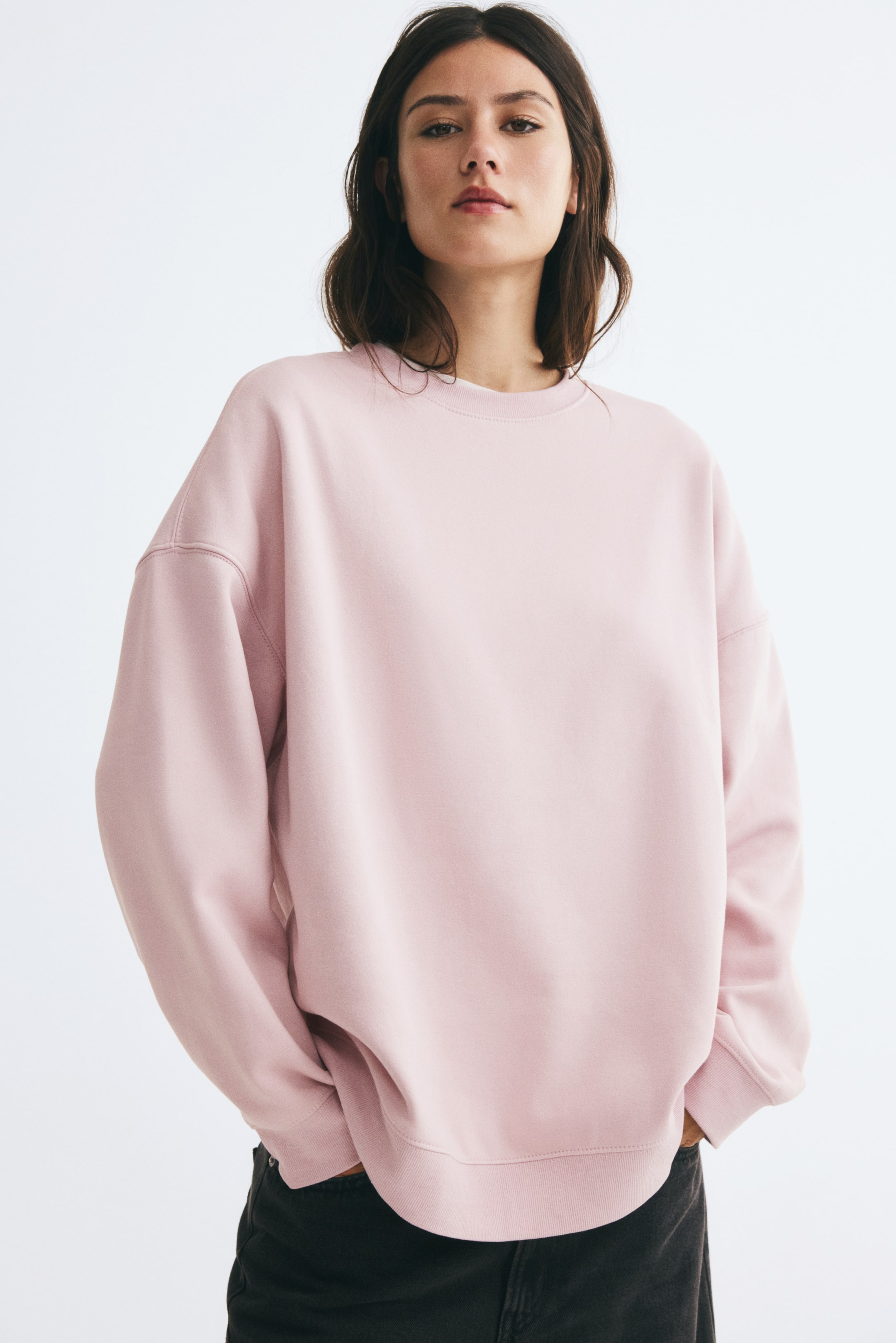 View larger image: The model is wearing a light pink oversized sweatshirt featuring a crew neckline, dropped shoulders, and ribbed trim at the collar, cuffs, and hem. It is styled with dark jeans, and the model is standing with hands in pockets.