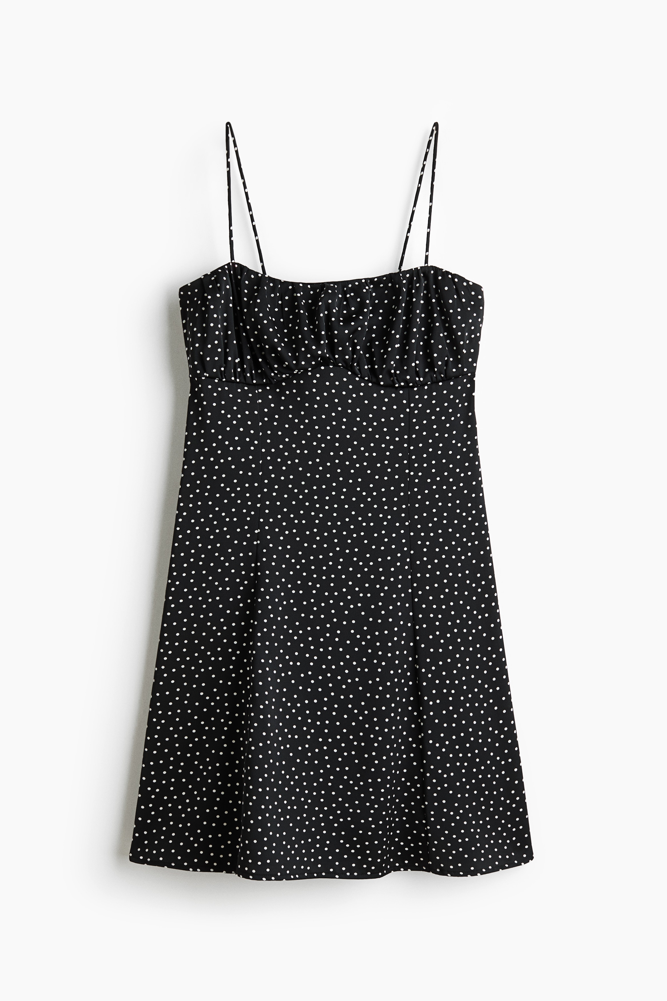 La modelo lleva un vestido negro de lunares, con escote recto, tirantes estrechos y el busto fruncido. El vestido se superpone sobre un top rosa intenso, dejando visibles los tirantes rosas y el ribete del escote.