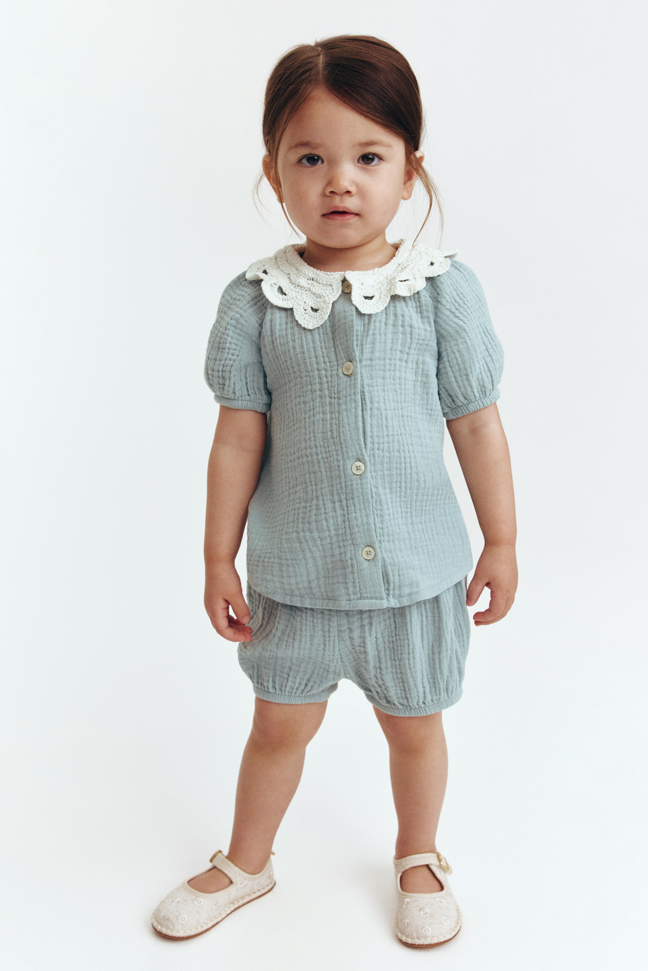 View larger image: Presenting a light blue-green two-piece set, showcasing a crinkled gauze texture. The top is a button-down shirt adorned with a large, scalloped white crochet collar and puffed short sleeves. The matching shorts feature gathered leg openings, adding to the ensemble's charm.