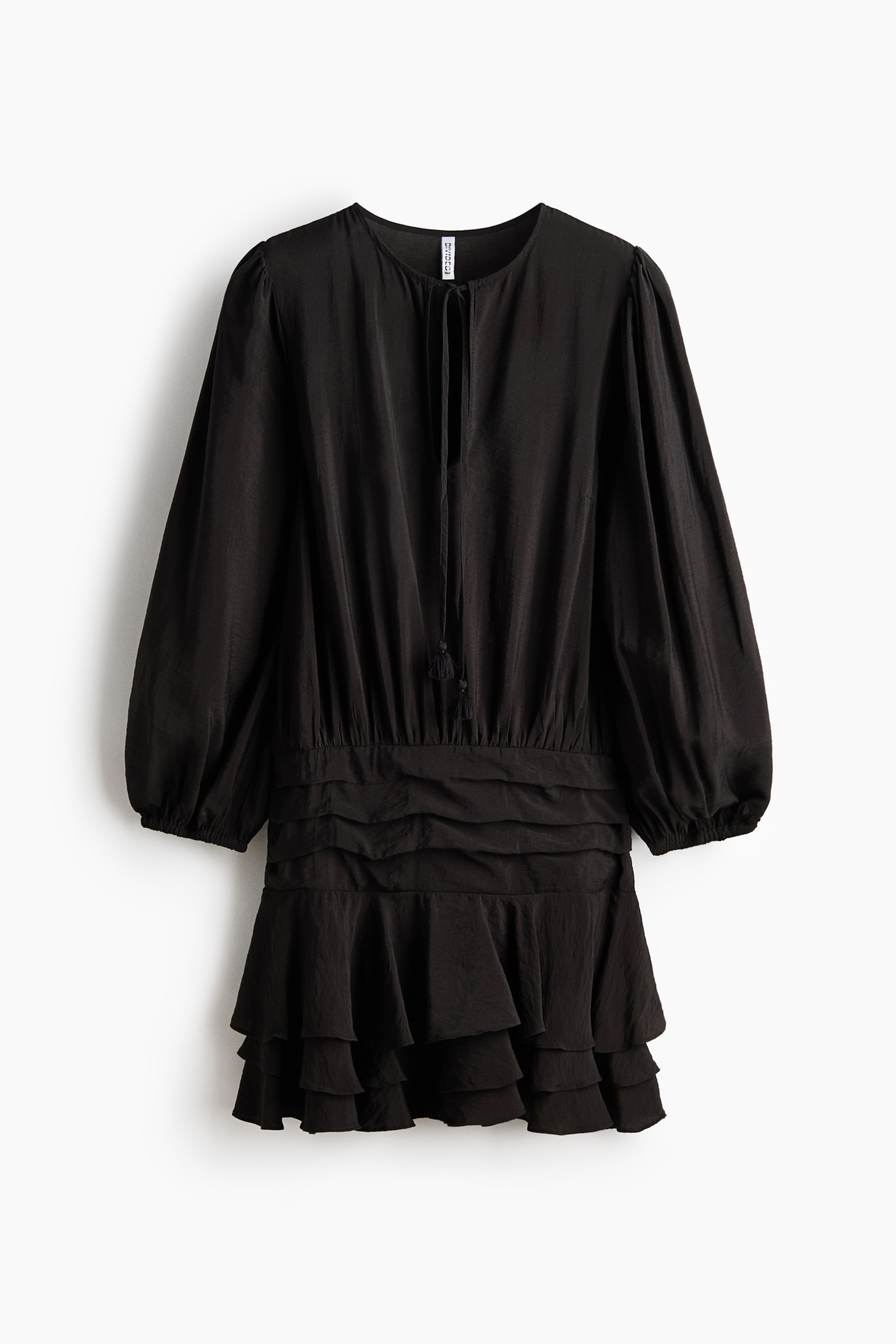 查看大圖: 此黑色連身裙正面展示，採圓領綁帶收口，綁帶末端綴以流蘇；長蓬袖配鬆緊袖口；腰部為鬆緊設計並帶有橫向抓褶；下擺為分層荷葉邊裙襬。