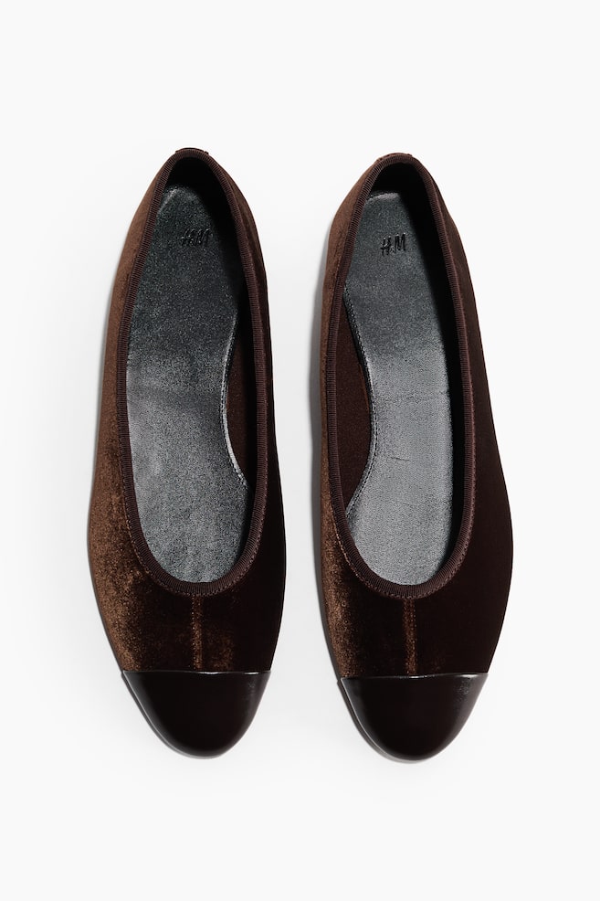 A pair of brown ballet pumps is being displayed, each shoe featuring velvet uppers and a rounded, dark brown patent leather toe cap. A thin brown ribbed trim outlines the opening, and a black inner sole lies inside. - 1
