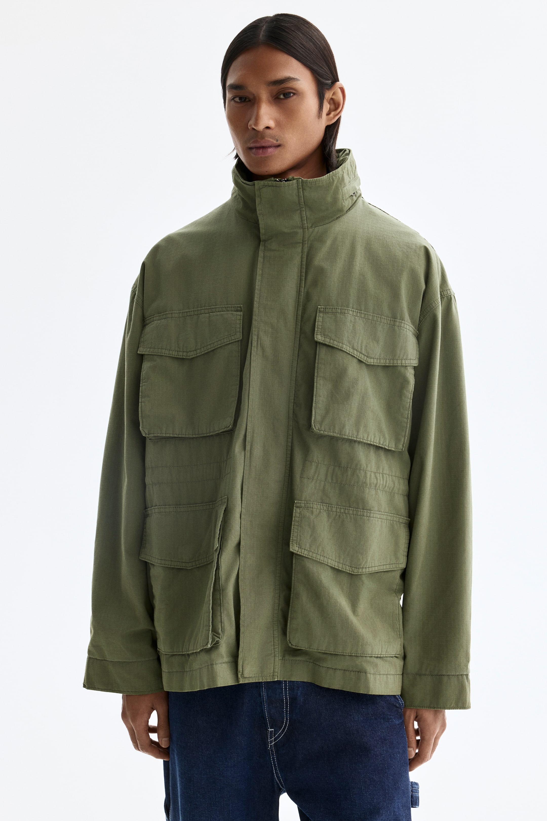 View larger image: An olive-green jacket is shown with a stand collar and four large front flap pockets. It features a relaxed fit with visible stitching details.