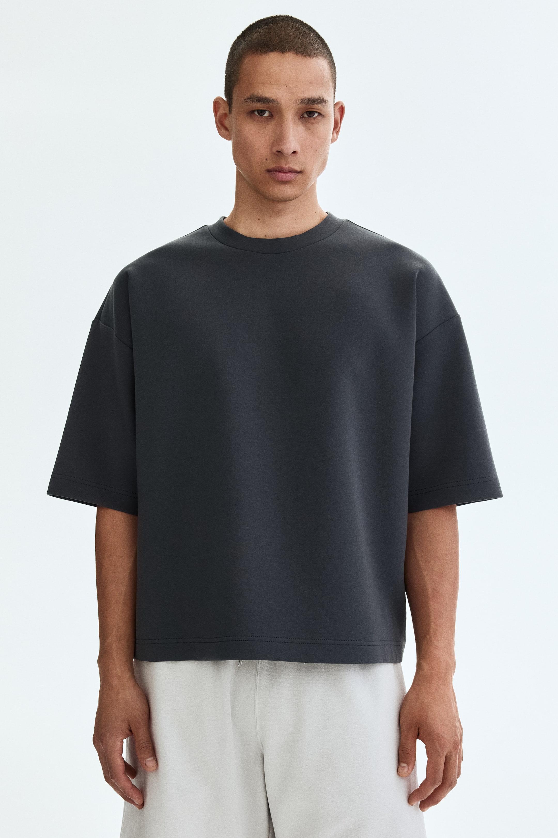 View larger image: A dark grey t-shirt is displayed, showcasing a crew neck and wide short sleeves with dropped shoulders. It offers an oversized fit and a straight hem.