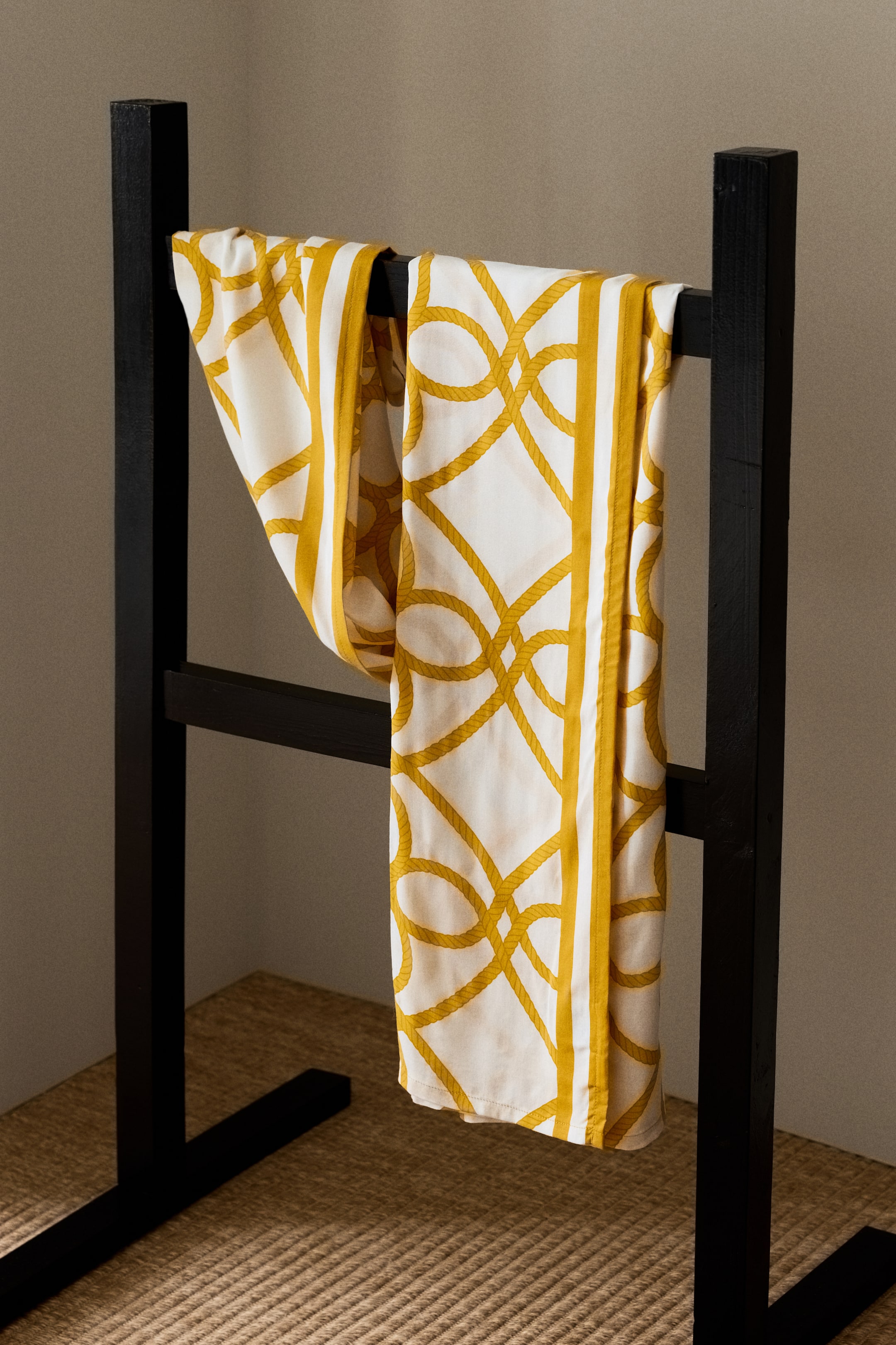 Agrandir l'image: Un sarong présente une base blanche avec un motif de corde dorée sur toute sa surface. Il est doté d'une bordure dorée solide le long de ses bords et est drapé pour mettre en valeur son tissu doux.