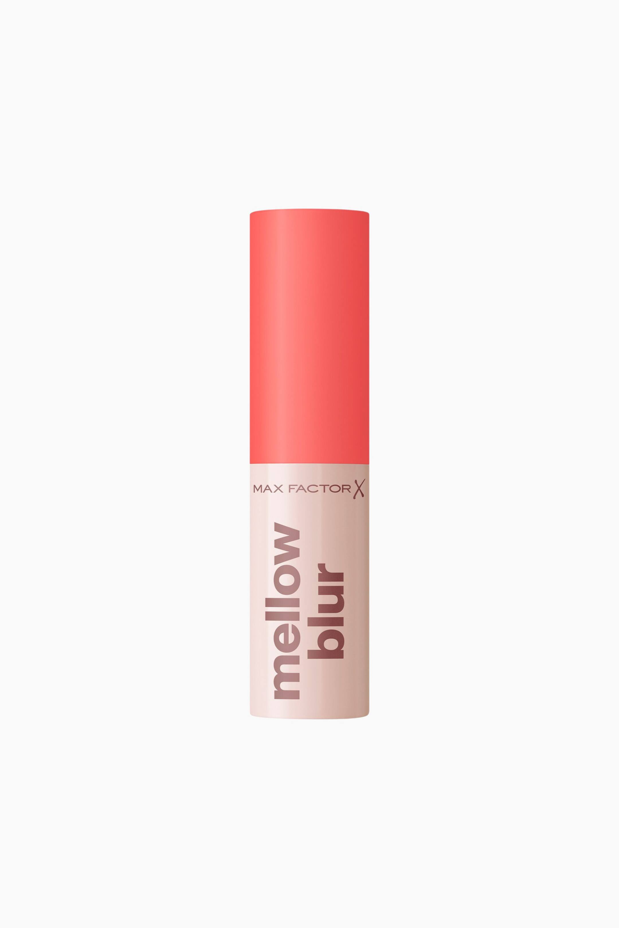 Vis større bilde: Mellow Blur Lipstick står loddrett i en rett forfra-visning, med en sylindrisk beholder og en matt korallrosa kork på toppen. Den lyse beige basen viser «MAX FACTOR X»-logoen horisontalt, med ordene «mellow blur» plassert vertikalt i mørkebrun, liten skrift.