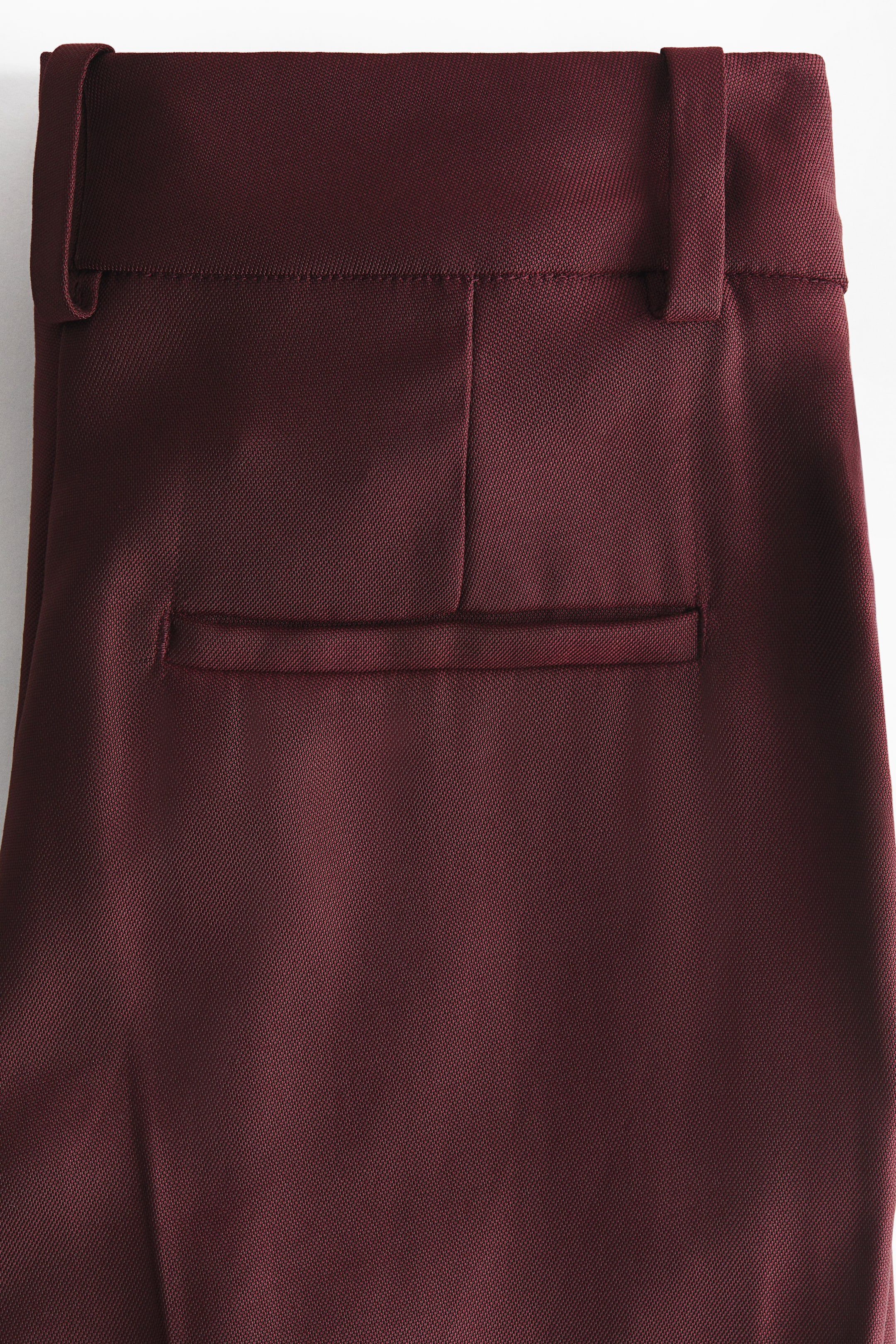 Agrandir l'image: Le pantalon bordeaux présente le haut du dos, avec une ceinture comprenant deux passants de ceinture et une seule poche passepoilée horizontale.