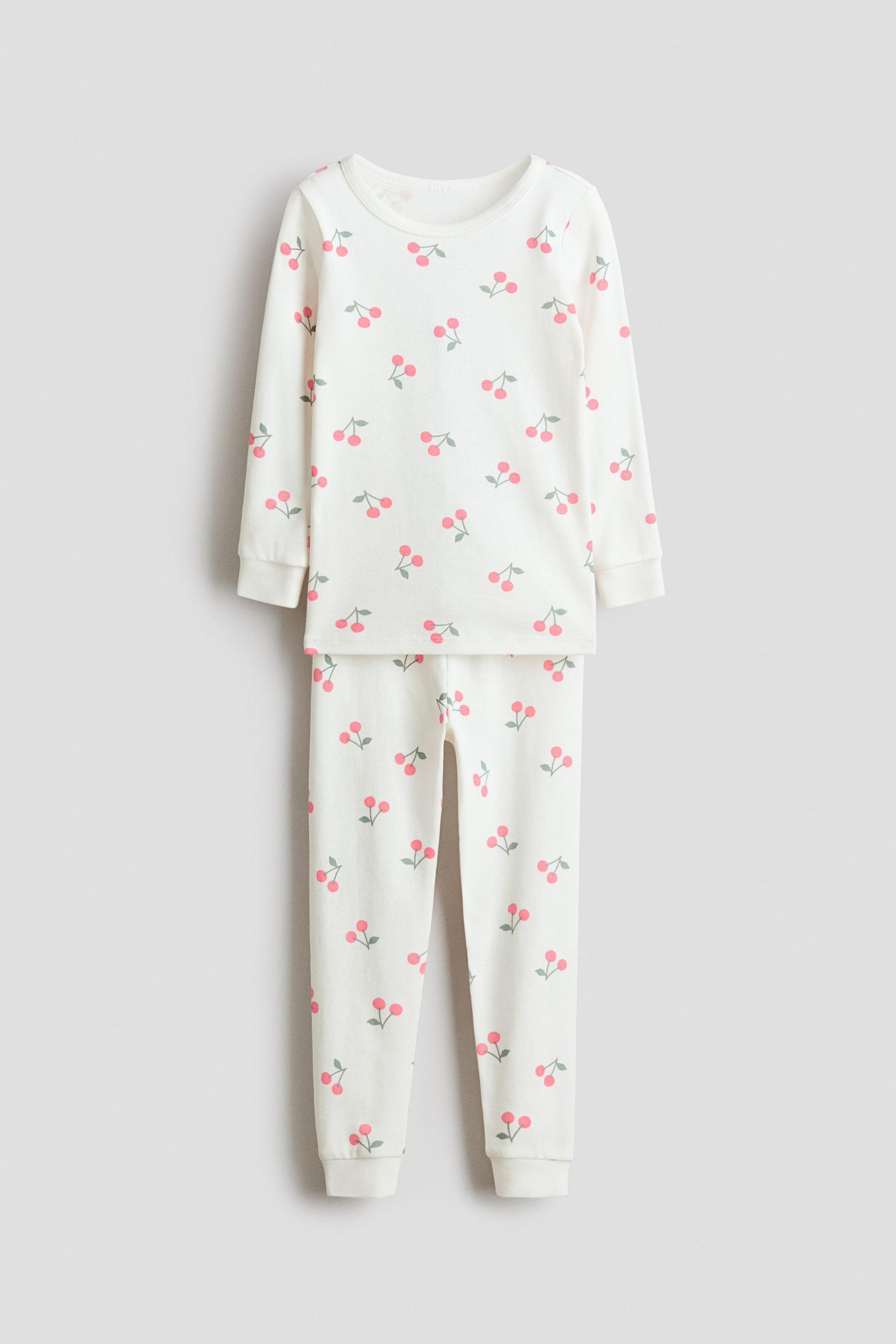 View larger image: Snug Fit printed cotton pajamas, shown from the front, feature a cream-colored long-sleeved top and matching long pants. Both pieces display a repeating pattern of pink cherries with green stems and are finished with ribbed cuffs at the wrists and ankles.