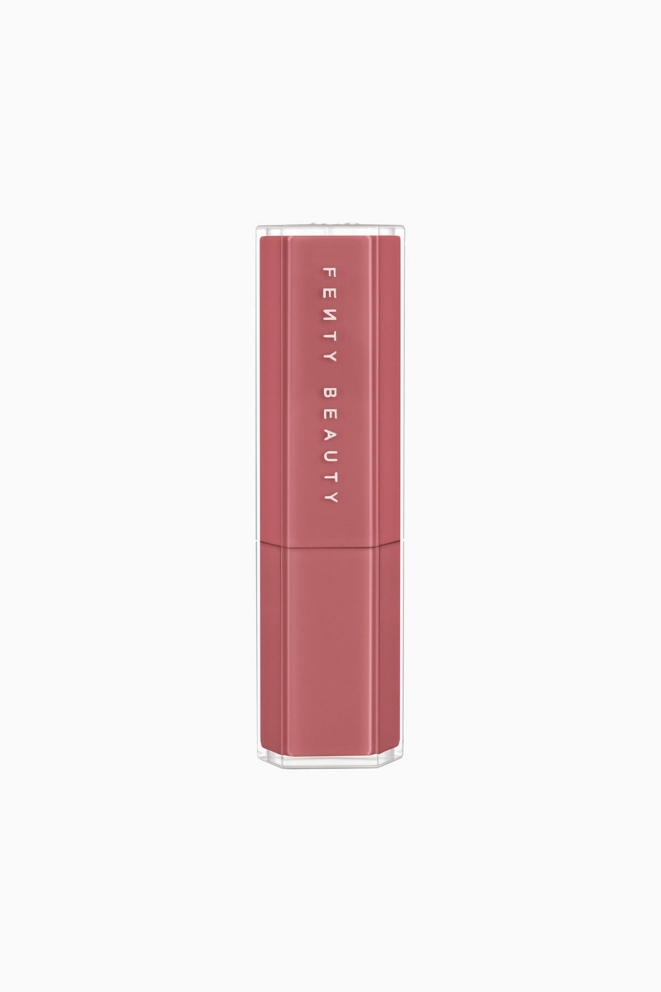 Näytä suurempi kuva: Gloss Bomb Stix High-shine Gloss Stick on pystyasennossa. Siinä on pölyisen ruusun sävyinen, kahdeksankulmainen kotelo, jota ympäröi läpinäkyvä ulkokuori. Brändinimi ”FE?TY BEAUTY” on painettu valkoisin kirjaimin pystysuunnassa korkin etupuolelle.