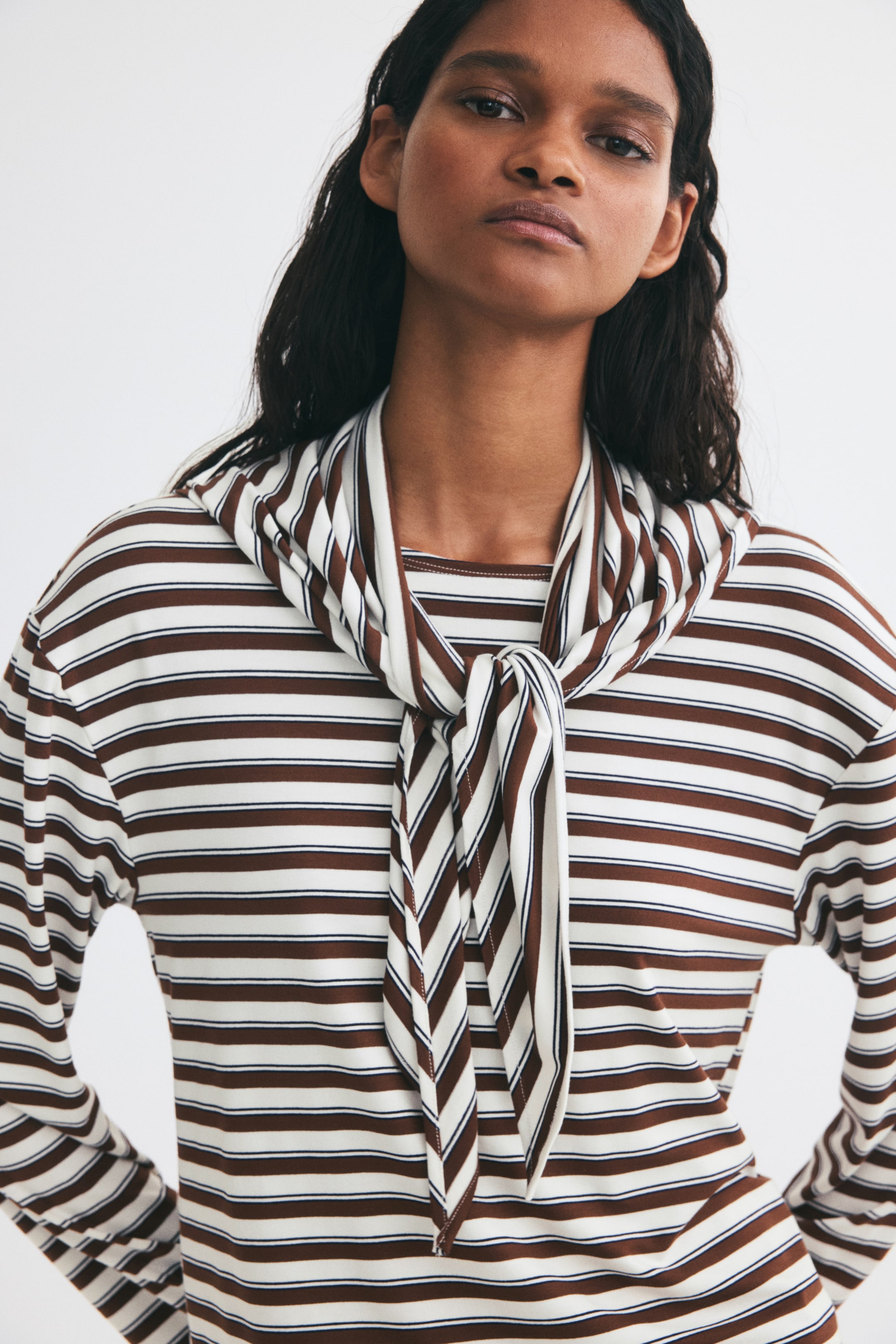 View larger image: The model is wearing a long-sleeved top with brown and white horizontal stripes, featuring an integrated pussy-bow scarf tied at the neck.