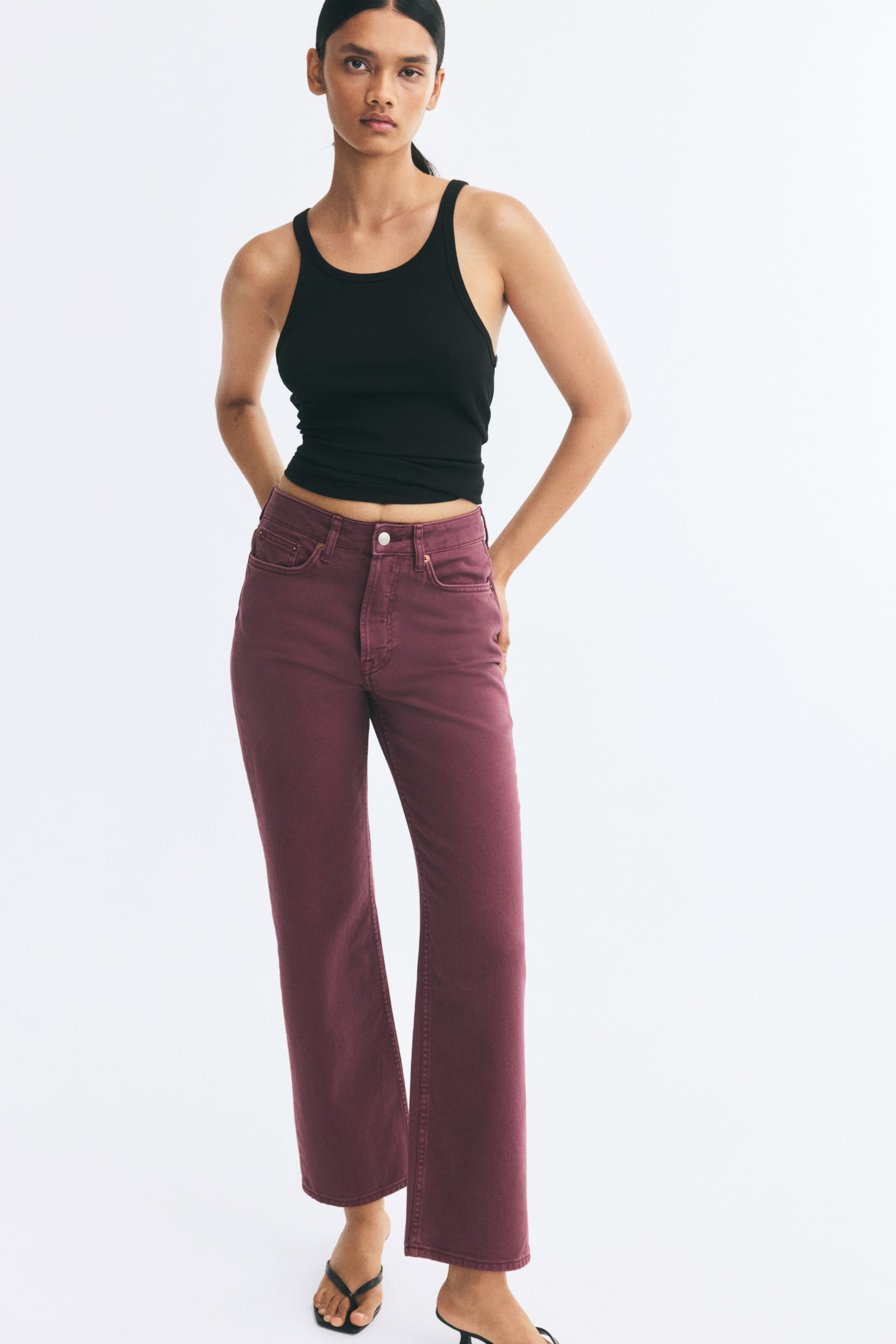 Visualizza immagine più grande: Jeans a vita alta, a gamba dritta, in un intenso colore prugna, indossati dalla modella, caratterizzati da un classico design a cinque tasche e da una silhouette strutturata. I jeans sono abbinati a un top nero a costine e a sandali neri con tacco.