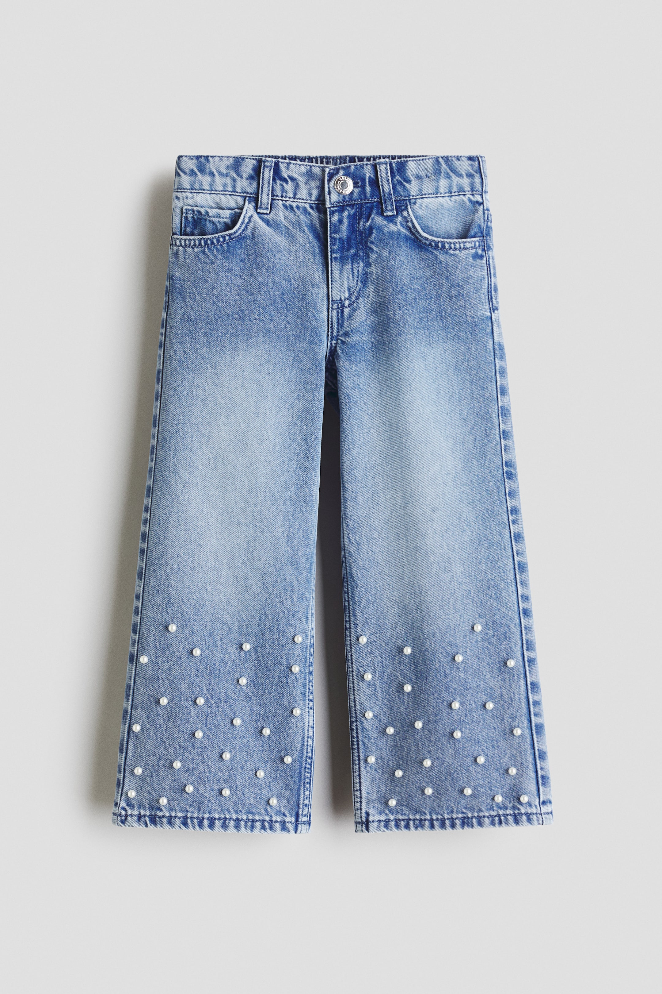 View larger image: Light blue denim wide-leg jeans are showcased from the front, featuring a faded wash, belt loops, and front scoop pockets. Small white pearls embellish the lower legs, scattered across the fabric.