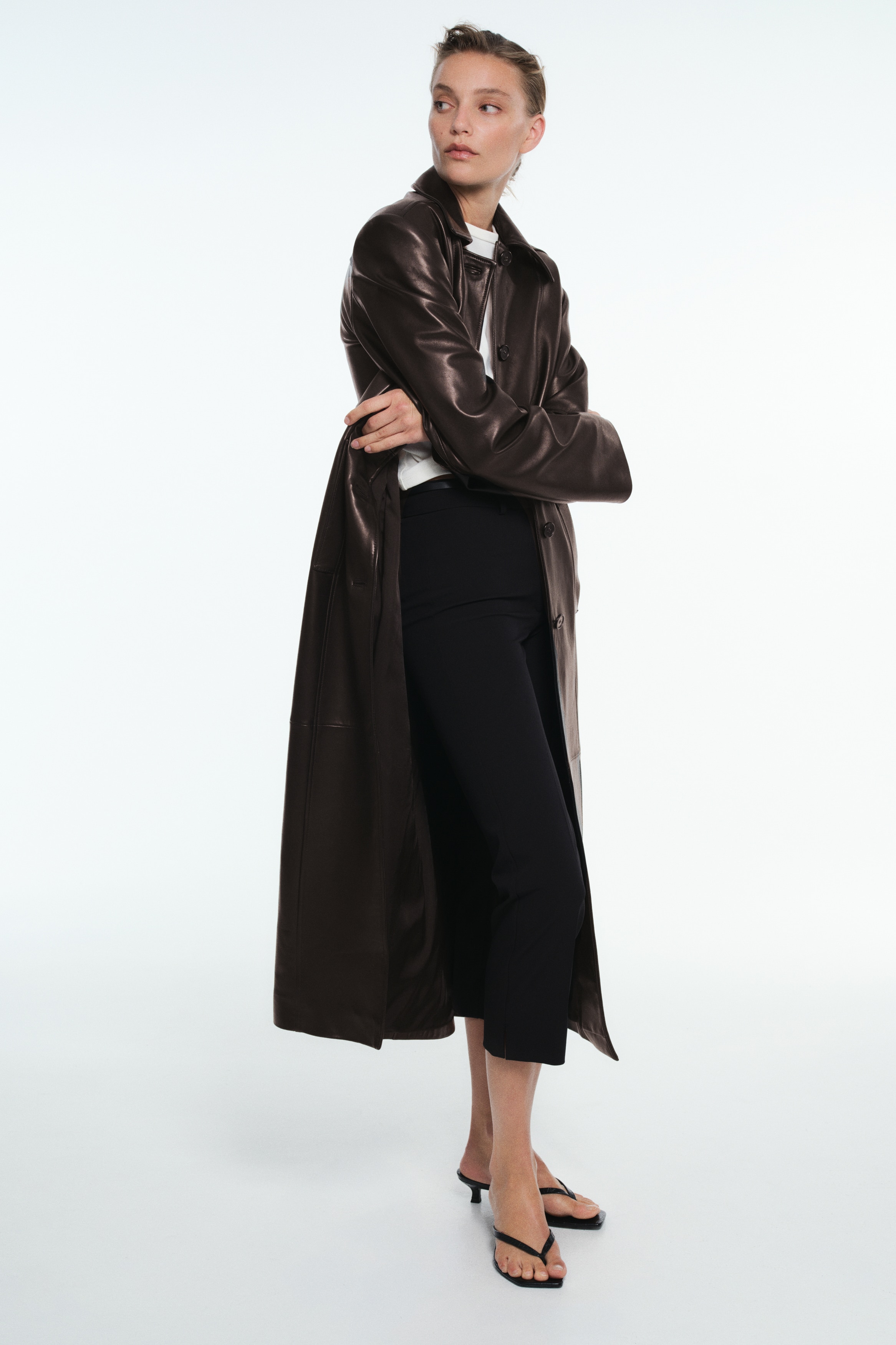 Black trousers are shown from the front, featuring a structured waistband with belt loops, a concealed front fastening, and sharp pressed creases running down the centre of each straight-cut leg.
