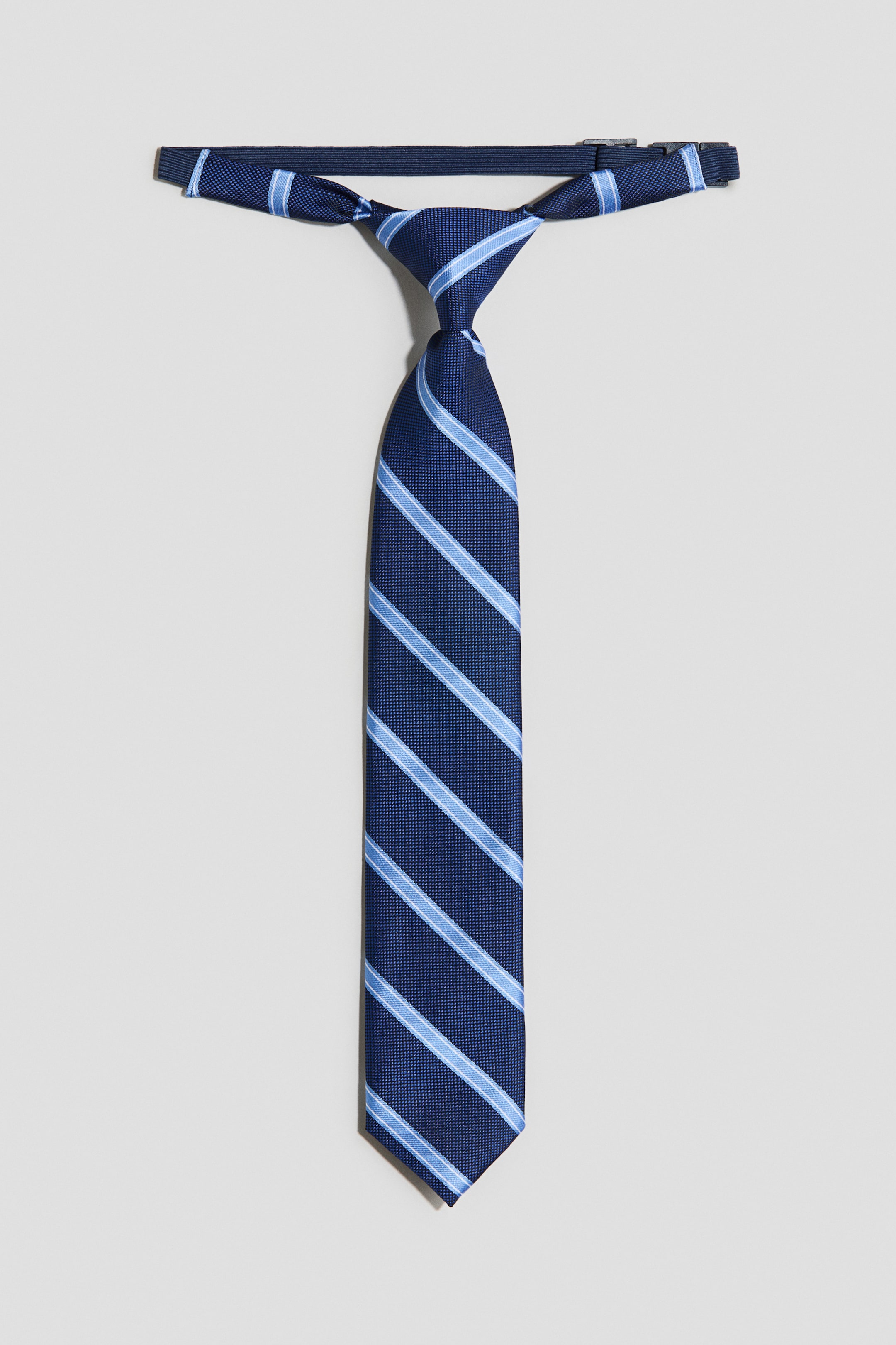 View larger image: A pre-tied tie, facing front, showcases navy blue woven fabric with diagonal light blue stripes. An adjustable, elasticated strap with a plastic fastener is positioned at the back.