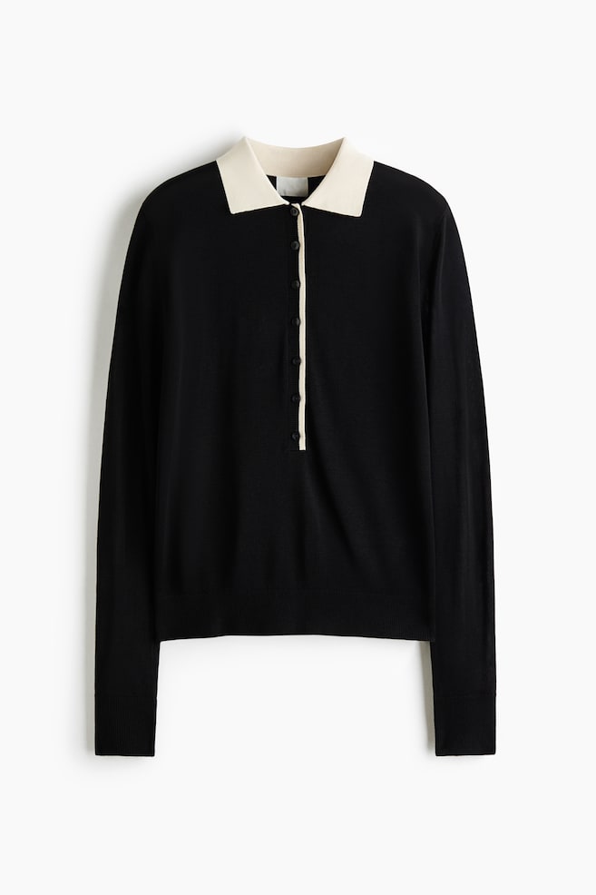 A black long-sleeved knit sweater is shown front-facing, featuring a contrasting cream-coloured polo collar and a partial button placket with a matching cream border. The garment showcases a fine-knit texture with ribbed cuffs and a ribbed hem. - 1