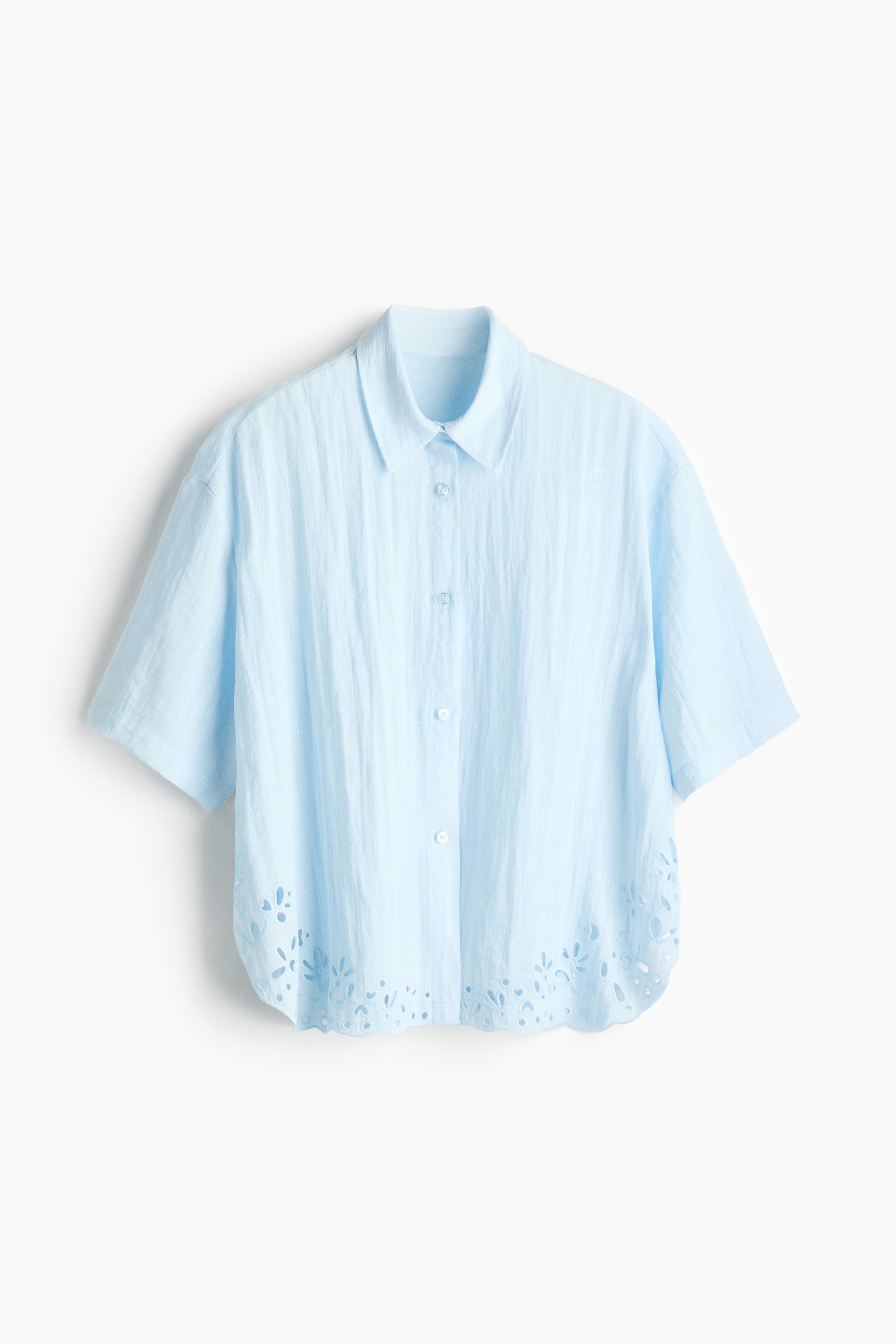 Ampliar la imagen: Una camisa de playa azul claro de corte holgado hecha de tela tejida presenta su parte frontal, con un cuello y botones en la parte delantera. Está diseñada con hombros caídos, mangas hasta el codo y un dobladillo curvo que muestra broderie anglaise.