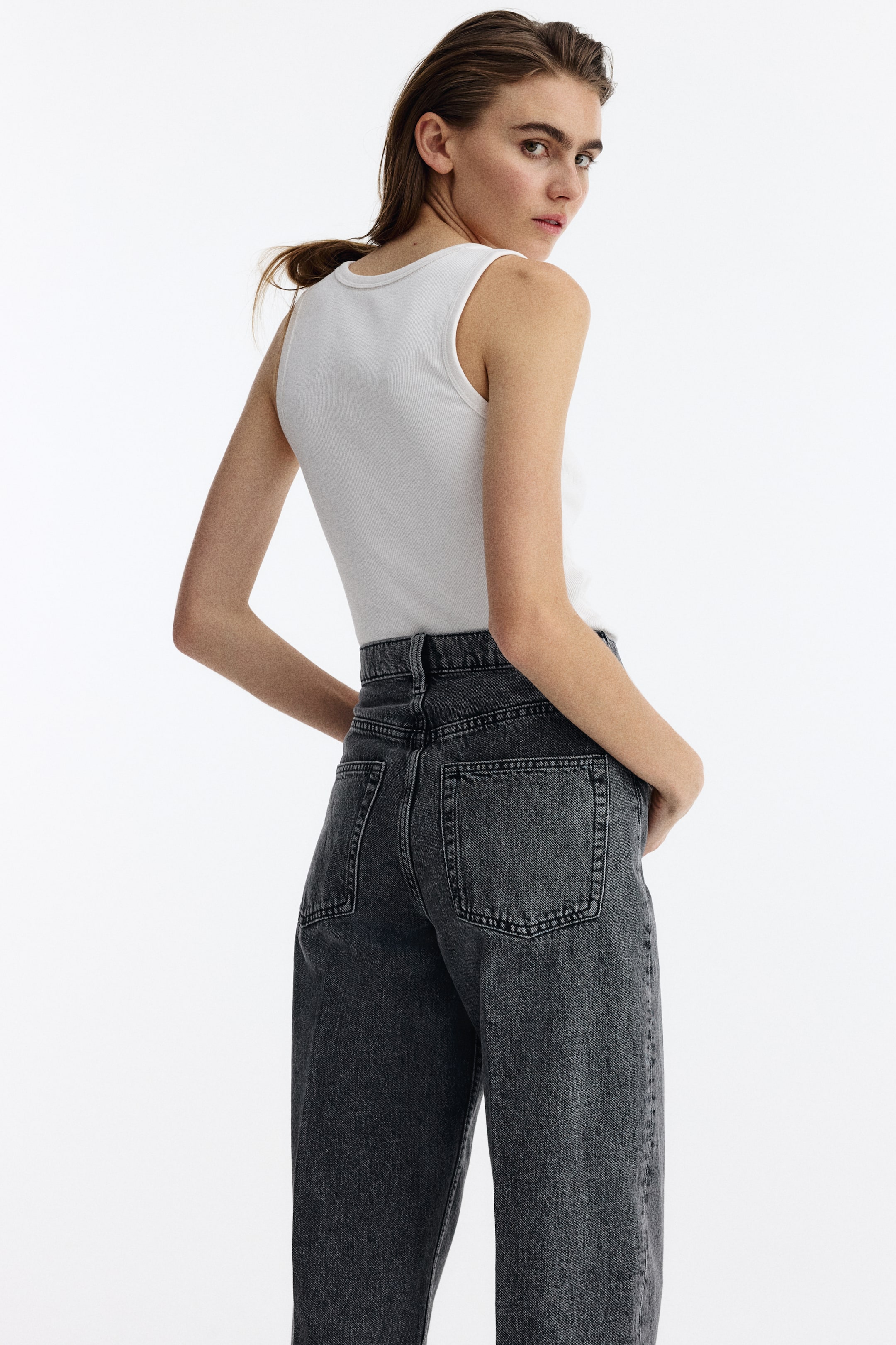 Voir une image plus grande: Les jeans gris foncé à 5 poches sont présentés de dos, mettant en valeur une taille haute et de grandes poches arrière rectangulaires. Les jambes volumineuses s'affinent vers l'ourlet, révélant des plis verticaux subtils, et semblent être de longueur cheville.