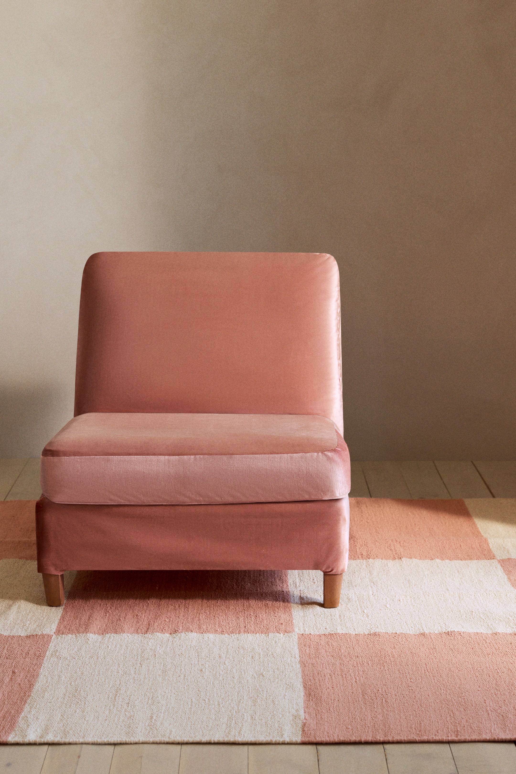 Agrandir l'image: Chaise en velours rose poussiéreux sans accoudoirs, présentée sous un angle avant-droit, avec un dossier et un coussin d'assise épais et arrondis, sa base assortie repose sur des pieds en bois courts et effilés.