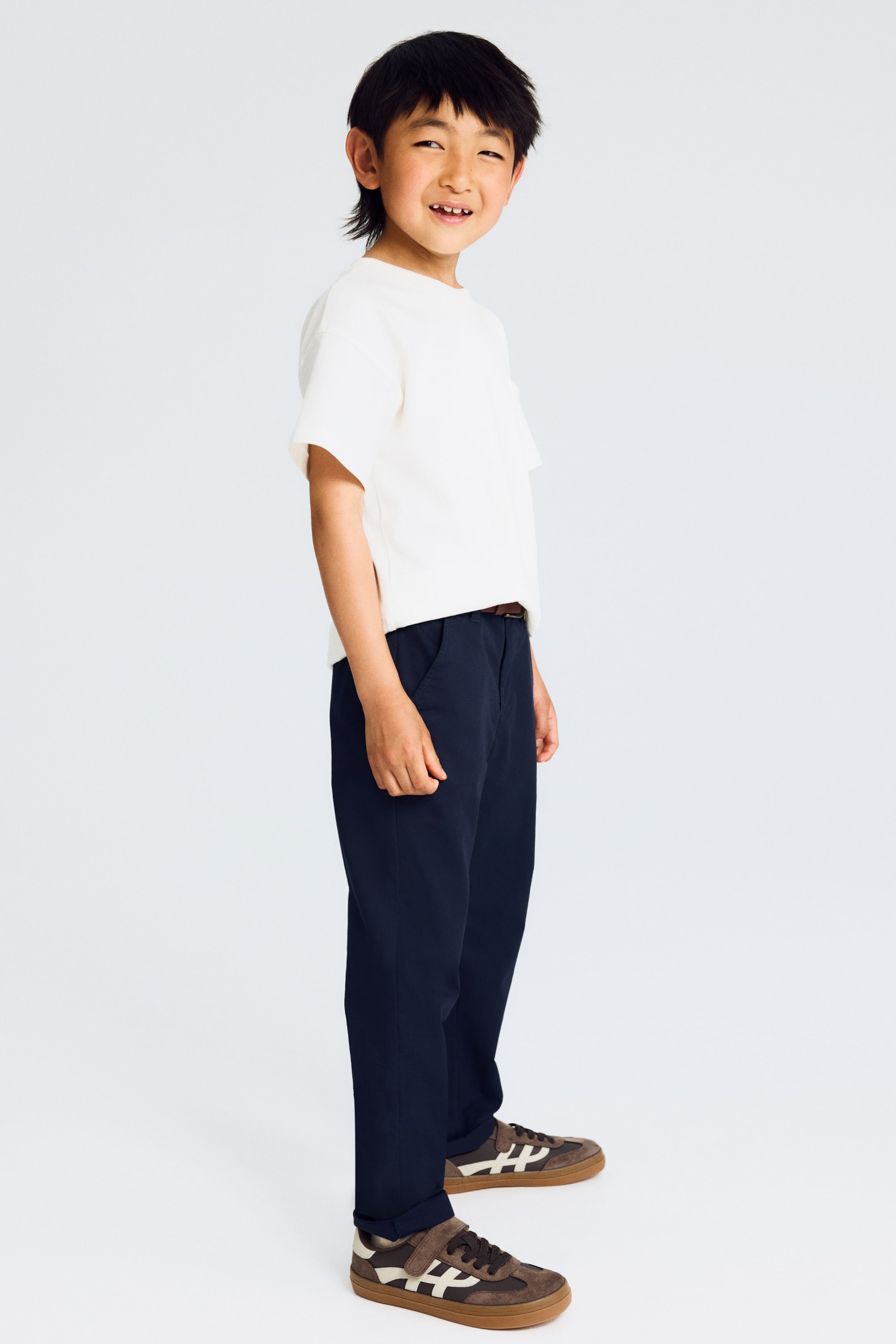 View larger image: Navy blue trousers are showcased from a side perspective, highlighting visible side pockets, a brown belt, and slightly folded hems.