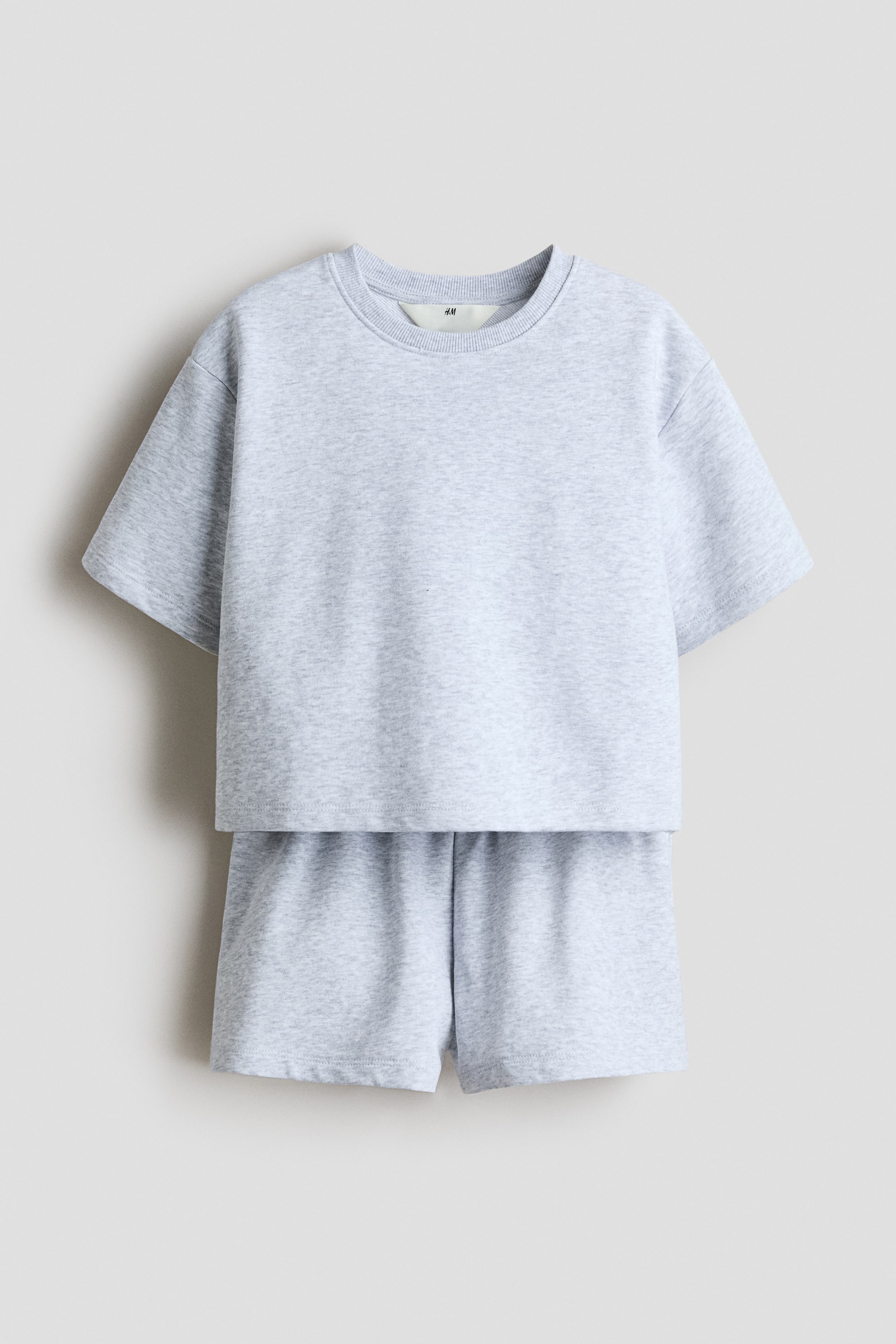 View larger image: The image showcases a heather grey two-piece ensemble from the front, comprising a T-shirt and coordinating shorts. The T-shirt features a round, ribbed neckline, dropped shoulders, and a straight-cut hem with short side slits. The shorts boast a covered elasticated waistband.
