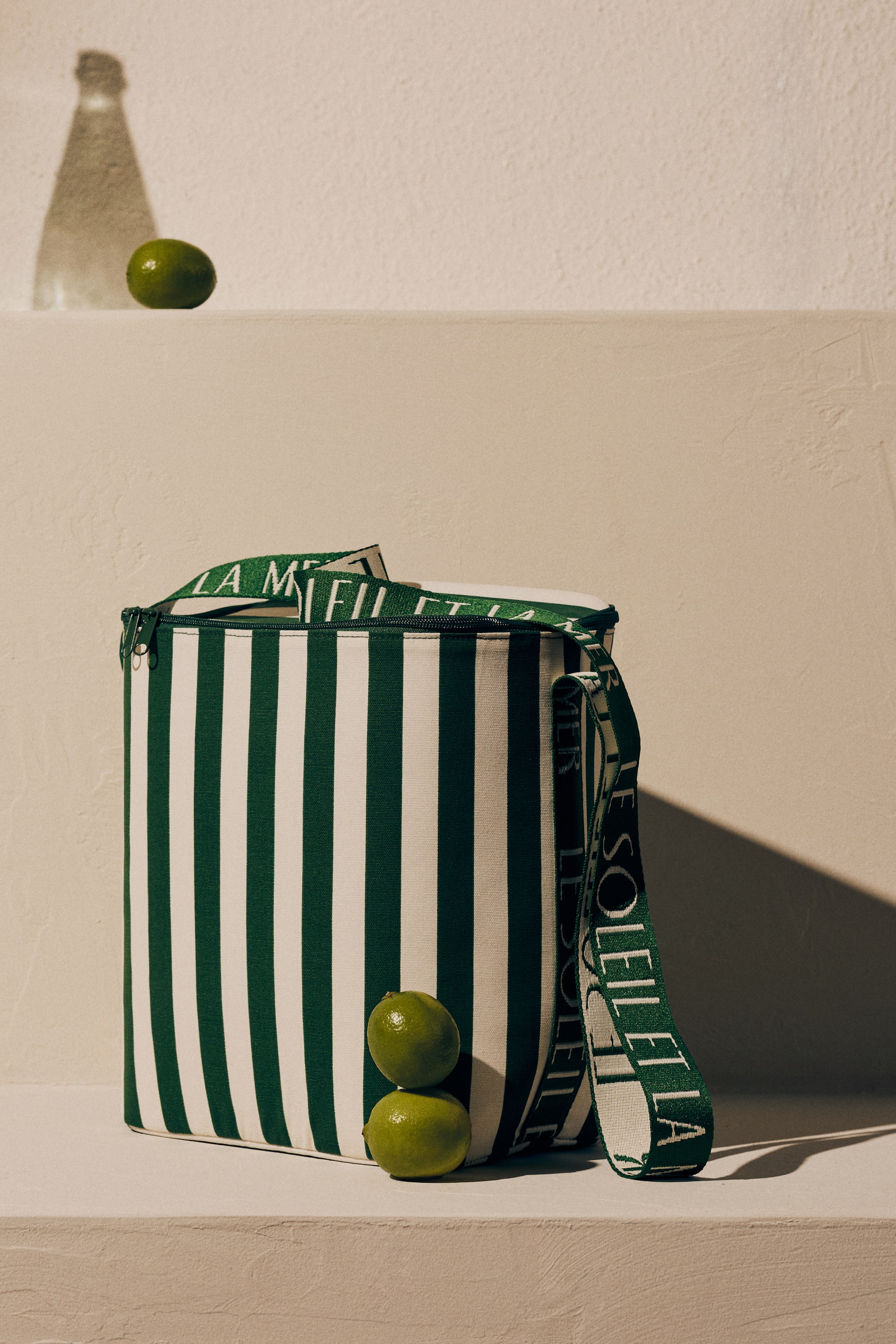 View larger image: A trendy bag showcases a green and white vertical striped design, displayed from the front. It features a zipper closure at the top and an adjustable shoulder strap with a jacquard-weave text motif.