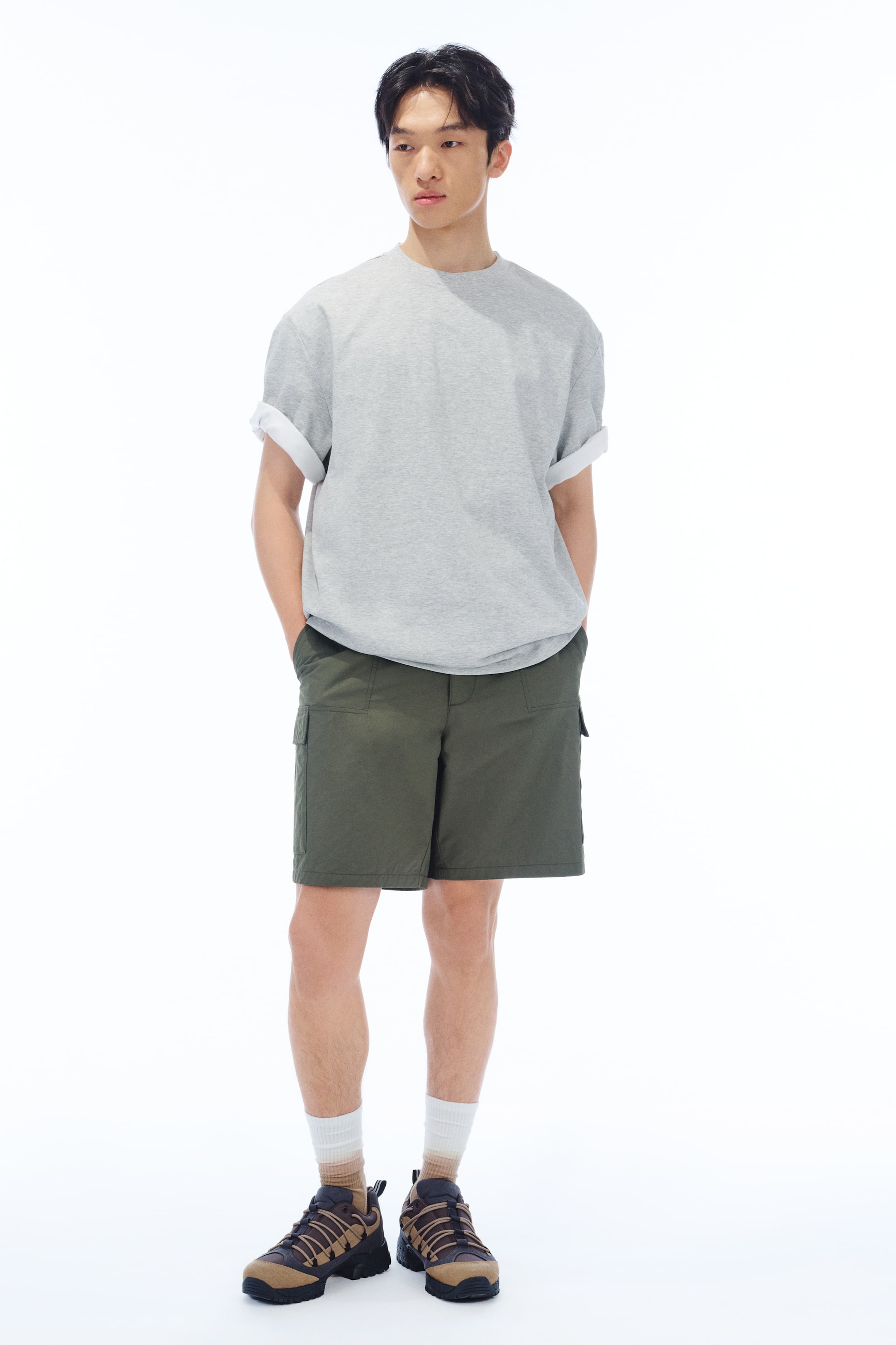 拡大画像を表示: モデルが着用している灰色のヘビーウェイトジャージーTシャツは、丸いリブトリムのネックライン、ドロップショルダー、カフ付きのショートスリーブ、ストレートカットの裾を備えており、ルーズフィットを演出しています。