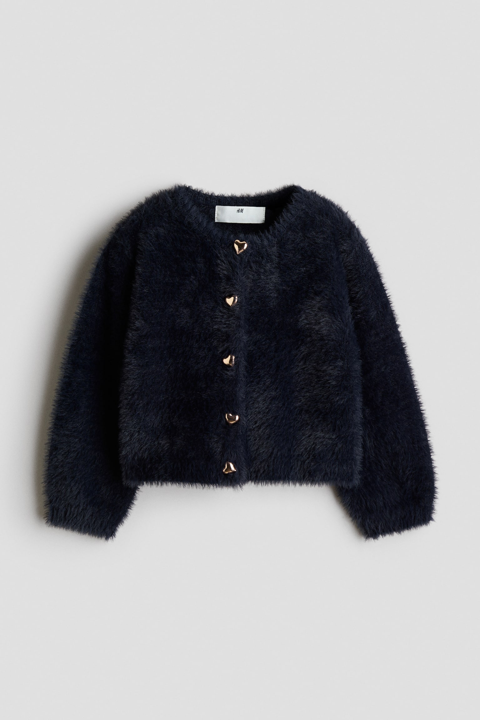 A dark navy blue cardigan in a soft, fluffy knit is shown from the front, featuring a round neckline and five gold-toned, heart-shaped buttons down the centre. The cardigan has long, slightly voluminous sleeves and a straight hem.