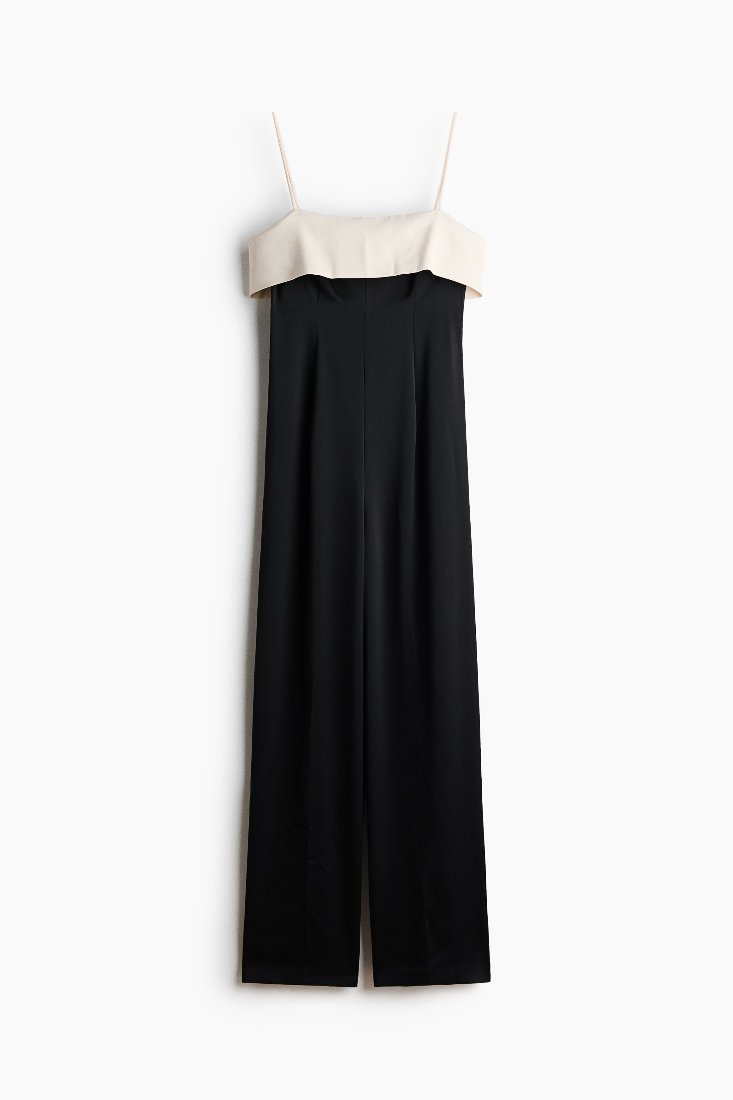 A straight-leg playsuit in woven fabric is being worn by the model, shown from a side-profile angle. The garment features a light-coloured, fitted top section with a wide foldover edge and thin spaghetti shoulder straps, paired with dark, high-waisted straight-leg trousers.