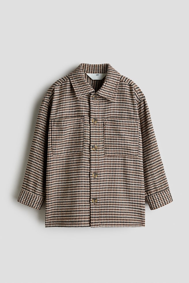 Ein oversized Overshirt mit braunem, schwarzem und beigem Hahnentrittmuster ist von vorne zu sehen und verfÃ¼gt Ã¼ber einen Umlegekragen, eine durchgehende Knopfleiste sowie zwei aufgesetzte Brusttaschen. Das Design umfasst Ã¼berschnittene Schultern und lange Ãrmel mit breiten Manschetten. - 1