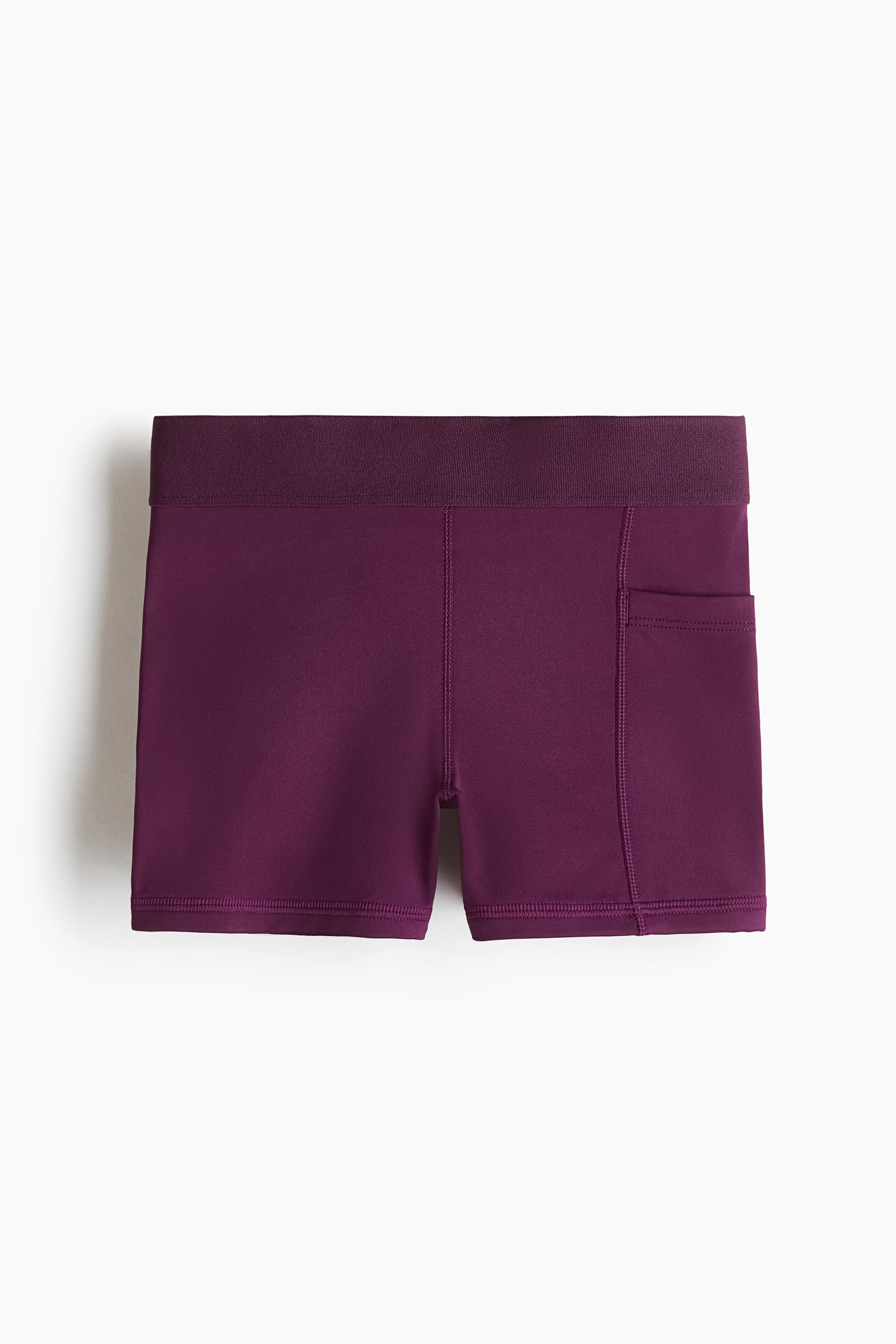 Ver imagen más grande: Los pantalones cortos deportivos morados presentan una amplia cinturilla acanalada de color morado oscuro y un tejido principal liso y sólido de color morado. Un bolsillo parche rectangular aparece en el muslo derecho, y las costuras planas recorren la parte delantera de las piernas y a lo largo de los lados.