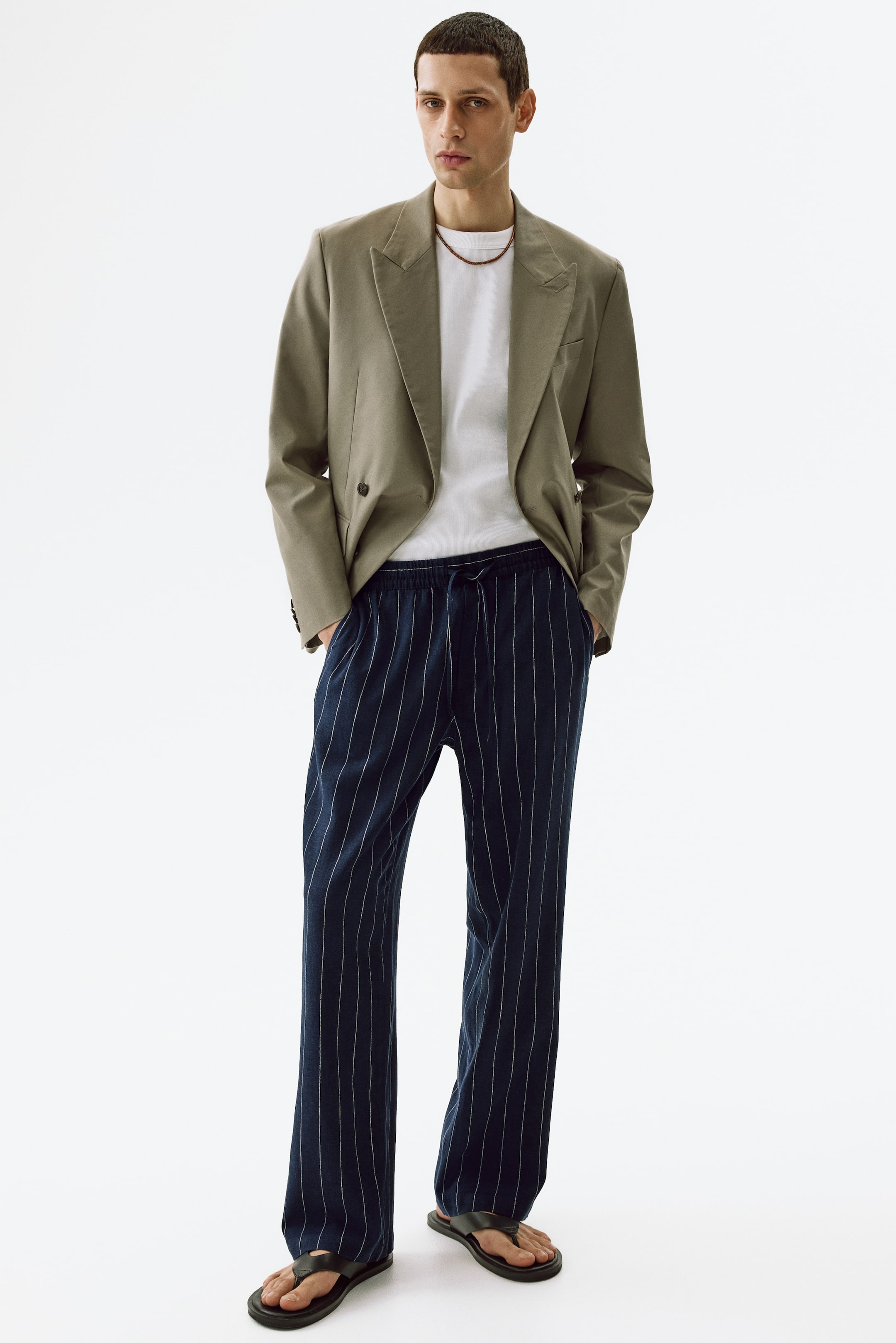 View larger image: The dark blue pinstripe trousers feature an elasticated drawstring waistband and a relaxed, straight-leg fit. They showcase thin white vertical stripes throughout and side pockets.