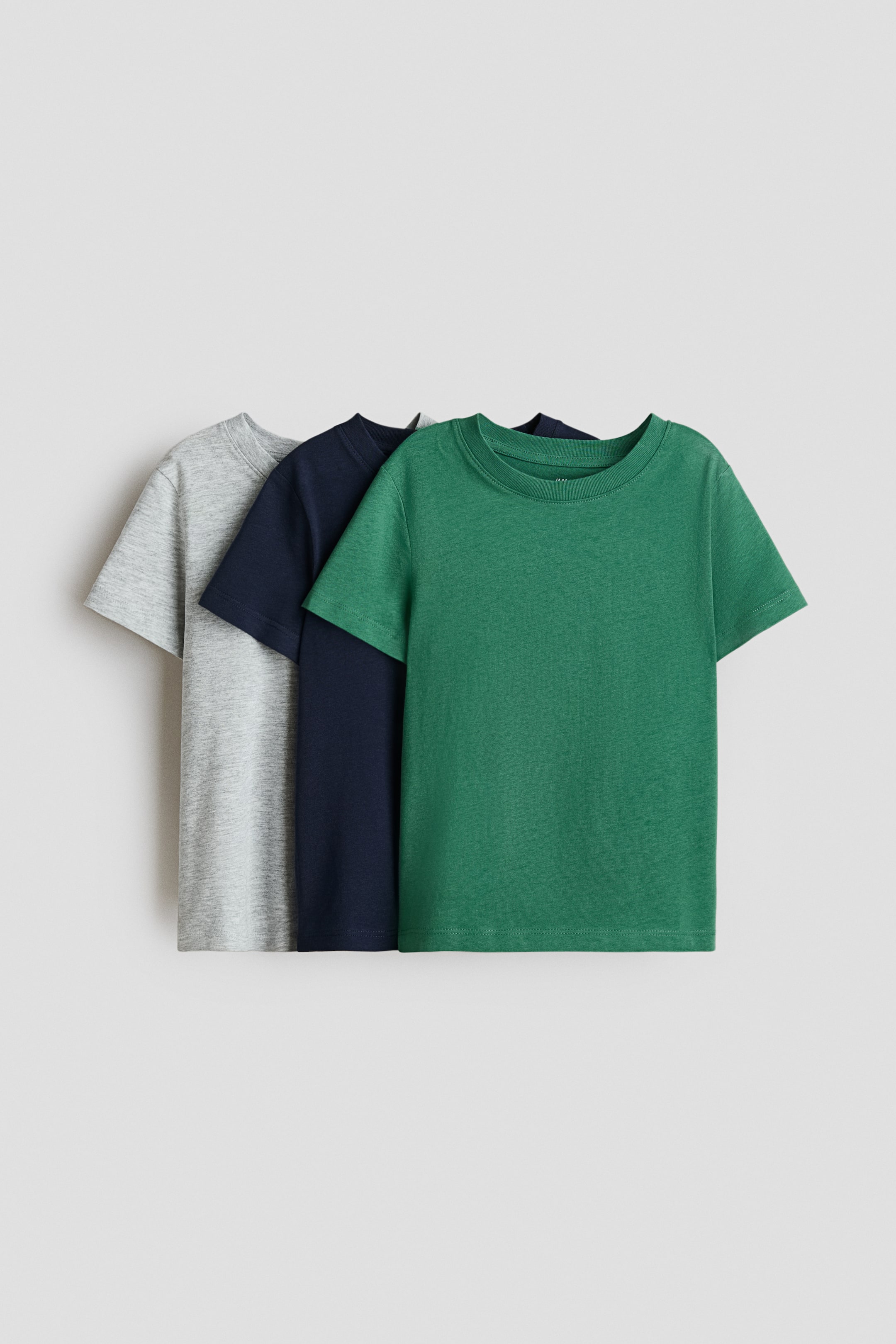 View larger image: Three t-shirts in soft cotton jersey are presenting their fronts, featuring a round, rib-trimmed neckline and short sleeves. The shirts are in green, navy blue, and light grey.