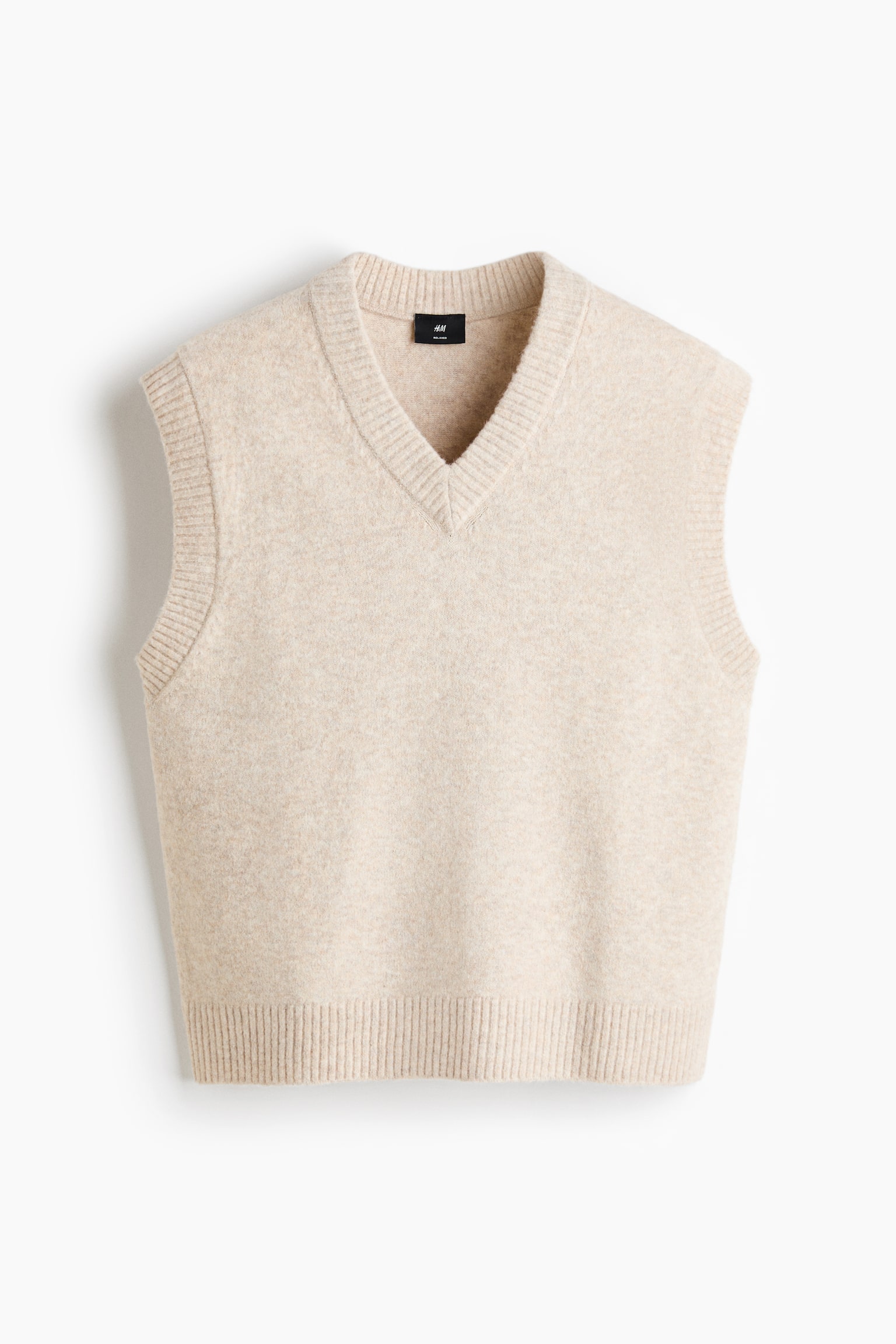 An oatmeal-coloured sweater vest is displayed from the front, featuring a ribbed V-neckline, ribbed armholes, and a ribbed hem, with a slightly fuzzy, knitted texture. - 1