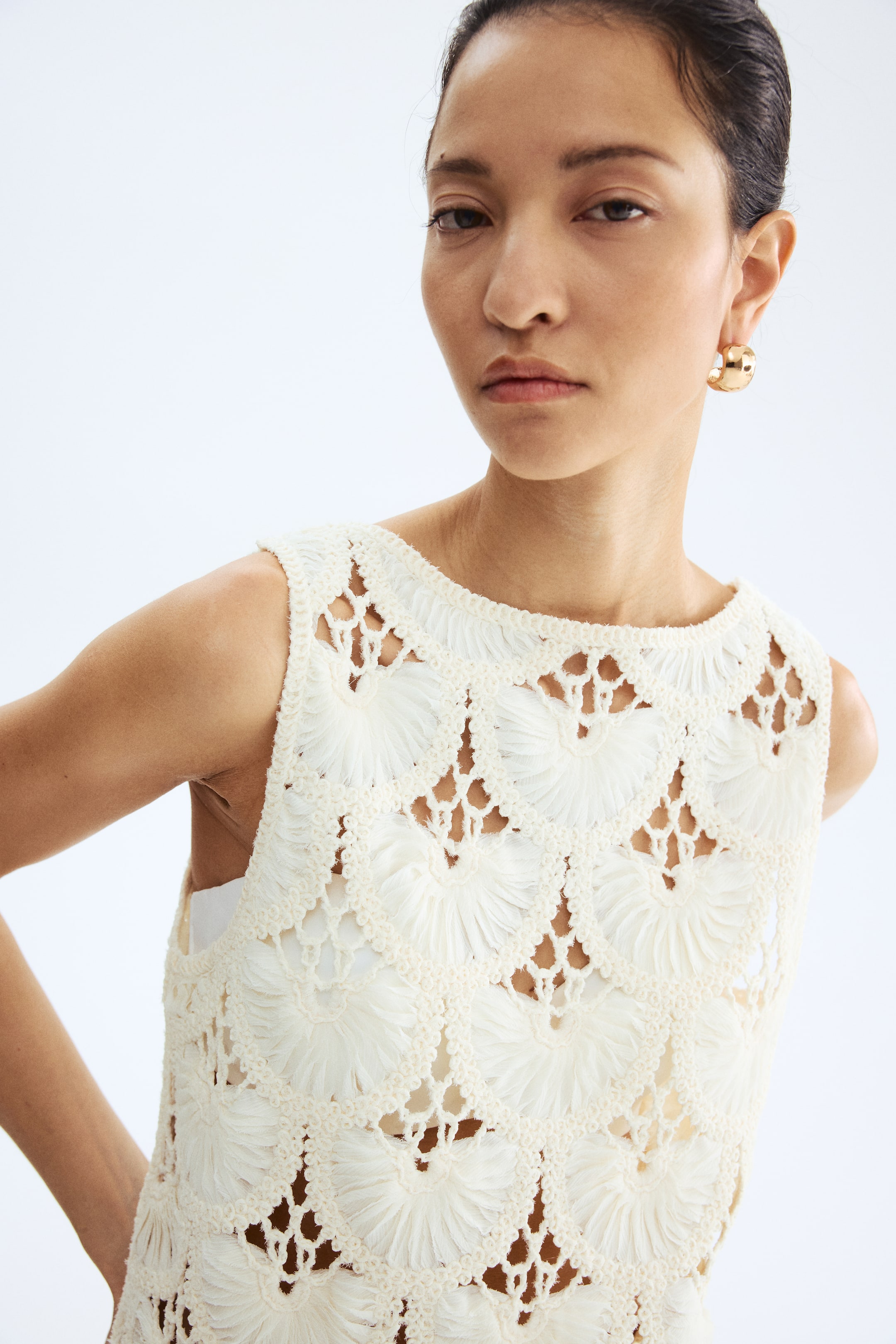 Größeres Bild anzeigen: Ein cremefarbenes ärmelloses Oberteil präsentiert ein aufwändiges Häkelmuster. Das Oberteil zeigt Lochmuster mit strukturierten, fächerartigen Kreismotiven und wird über einem weißen Unterhemd getragen.