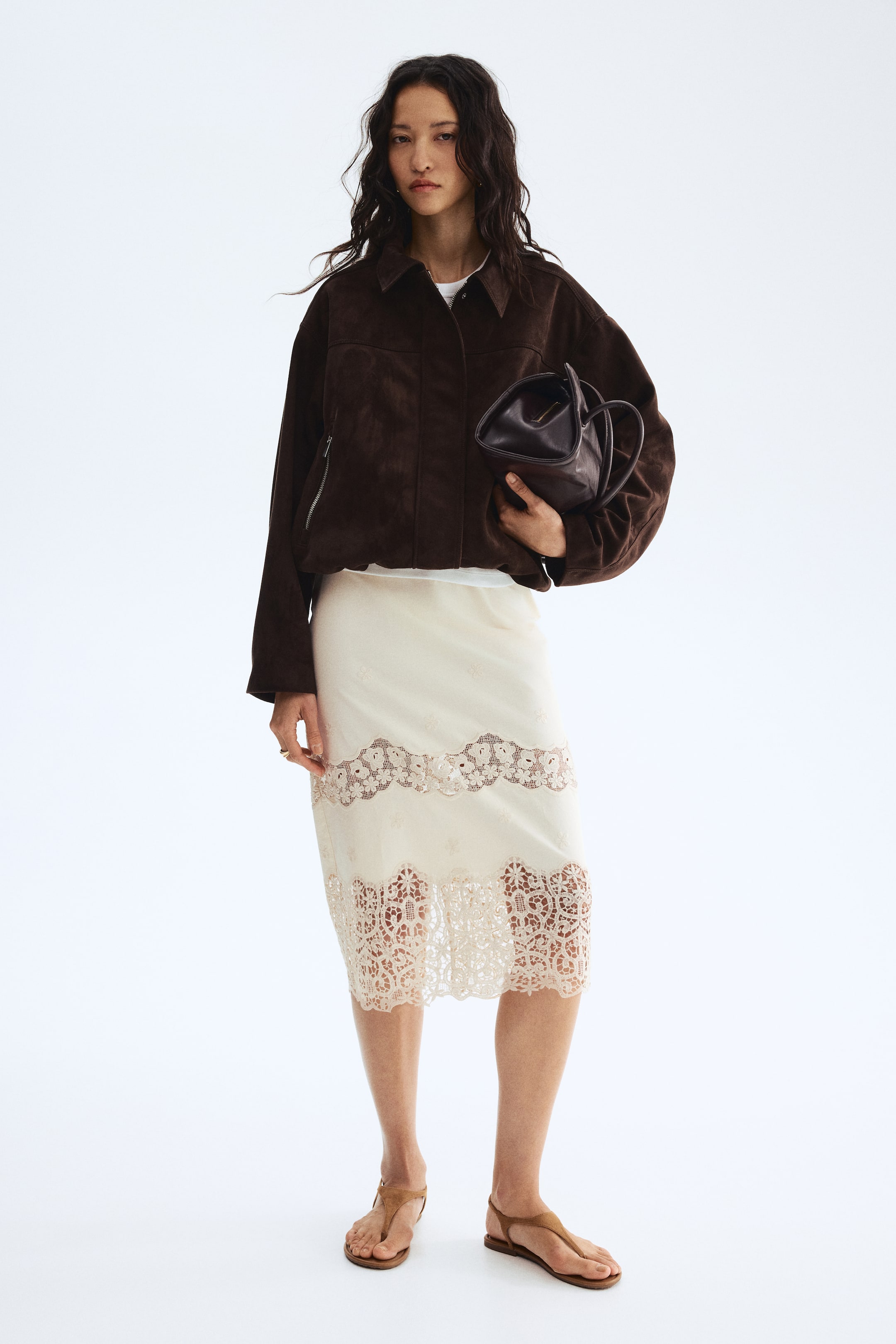 הצגת תמונה גדולה יותר: הדוגמנית לובשת חצאית באורך הברך מבד כותנה בהיר עם קטעי תחרה רקומים בשוליים, יחד עם ז'קט וחולצה.