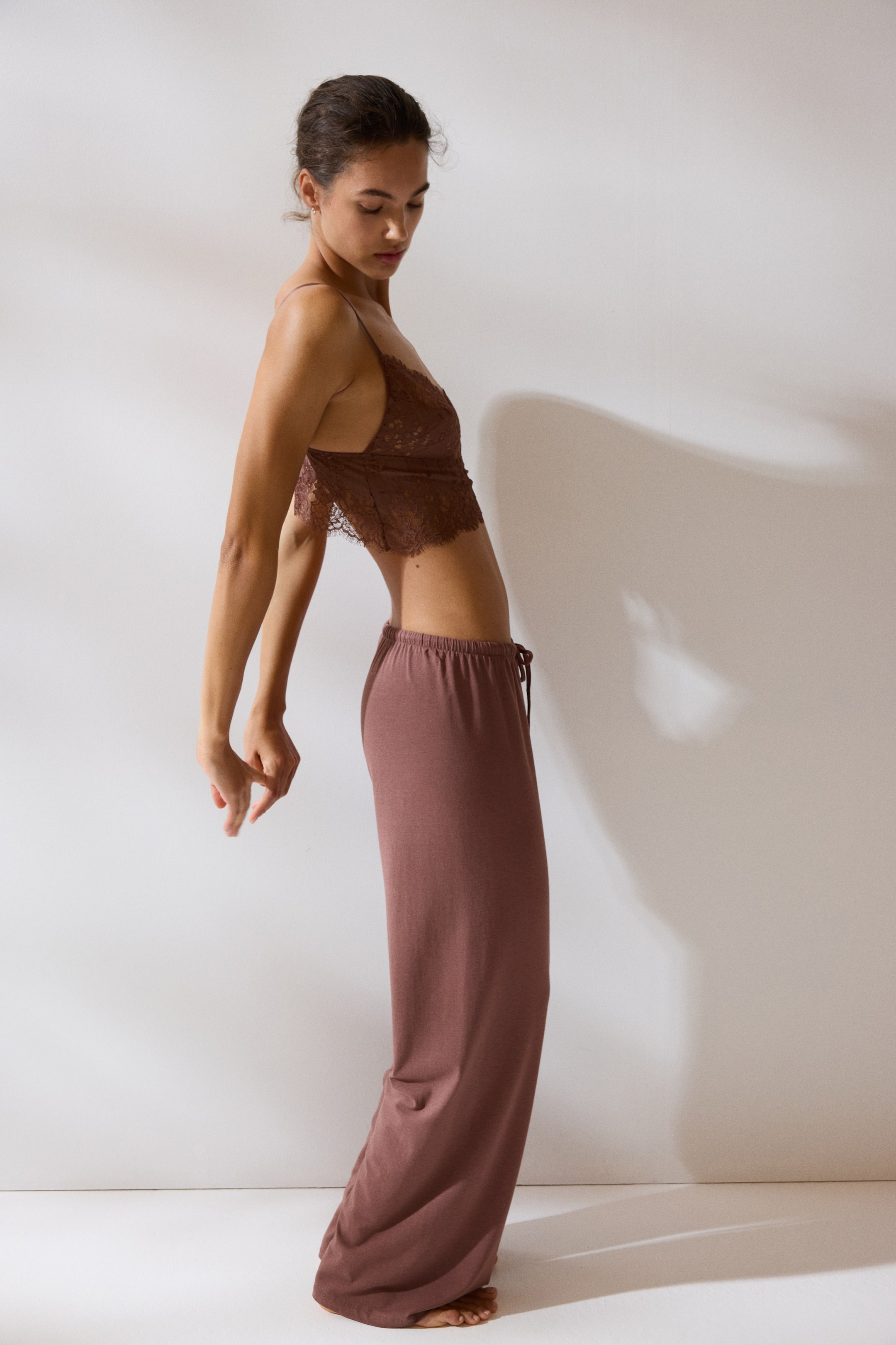 View larger image: The model is wearing loose-fit pyjama bottoms in a subtle reddish-brown shade, crafted from soft cotton and viscose jersey. These pyjamas come with an elasticated, drawstring waist and gracefully gather at her bare feet.