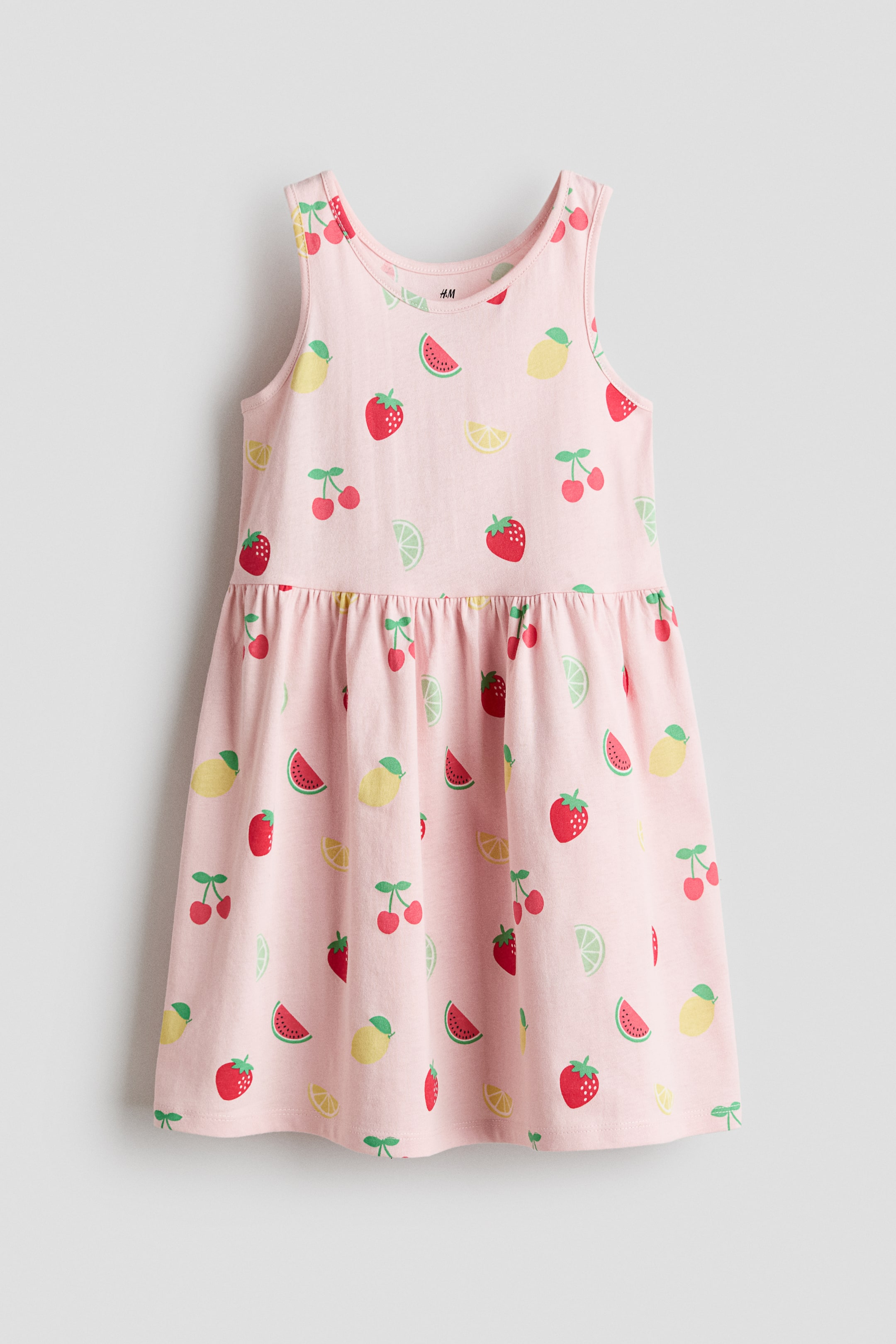 View larger image: A sleeveless dress in soft cotton jersey shows the front. It features an all-over fruit print on a light pink background, a round neckline, a gathered seam at the waist and a flared skirt.