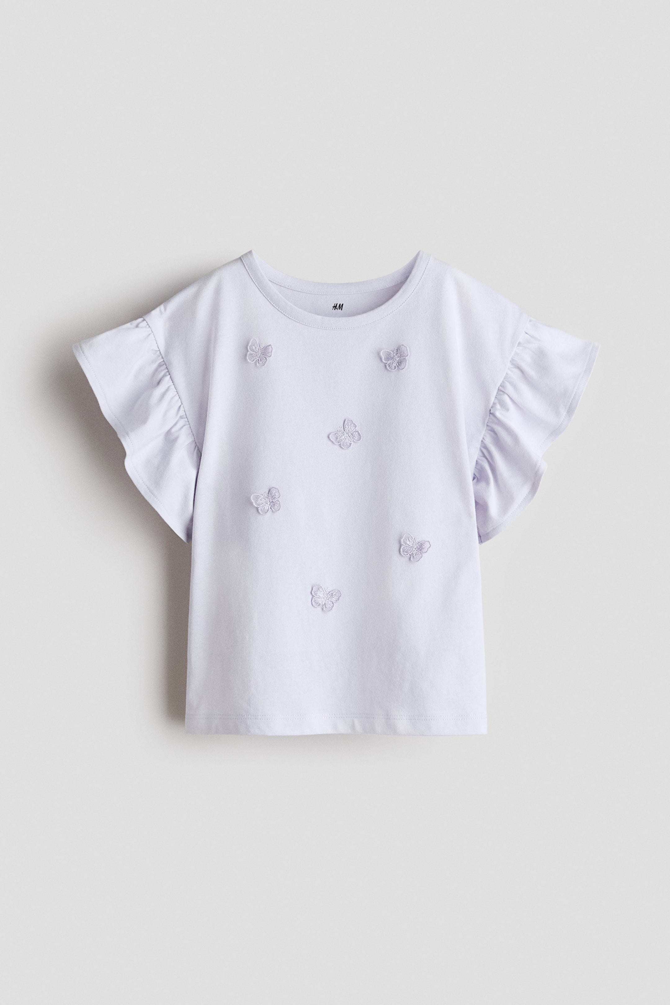View larger image: A light purple t-shirt is showcasing its FRONT, with a round neck, ruffled cap sleeves, and embroidered butterfly appliques spread across the front.