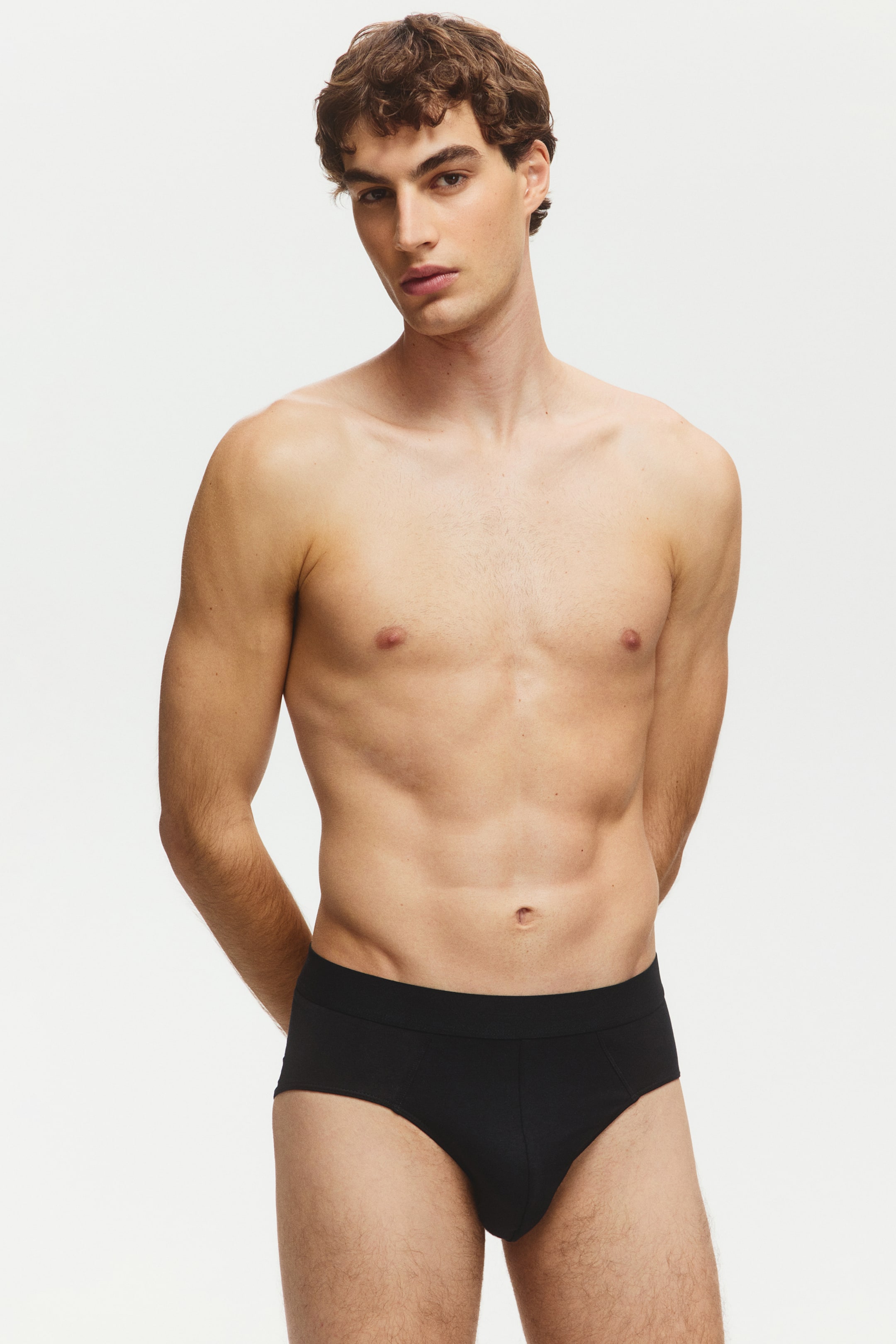 Ver imagen más grande: Los calzoncillos negros para hombre se llevan puestos, con una amplia cintura cubierta de la misma tela y una bolsa frontal contorneada, ajustándose estrechamente al cuerpo desde un ángulo frontal.