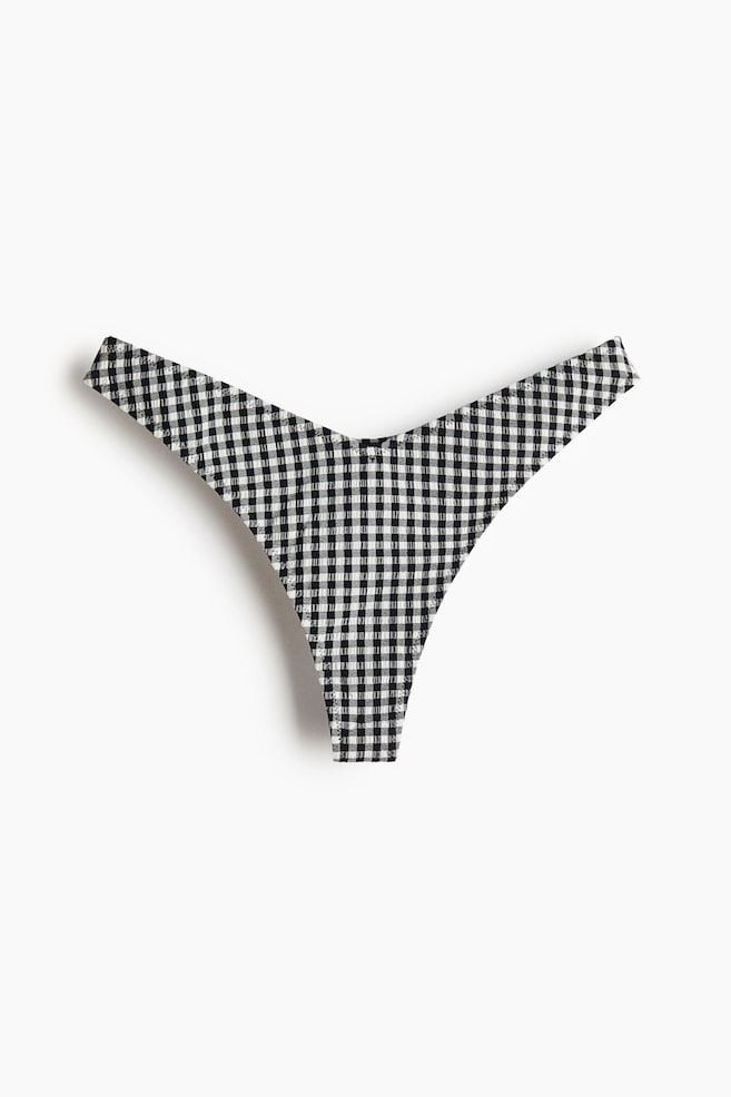These fully lined thong bikini bottoms showcase a black and white gingham pattern. They feature a low, V-shaped waistline at the front. - 1