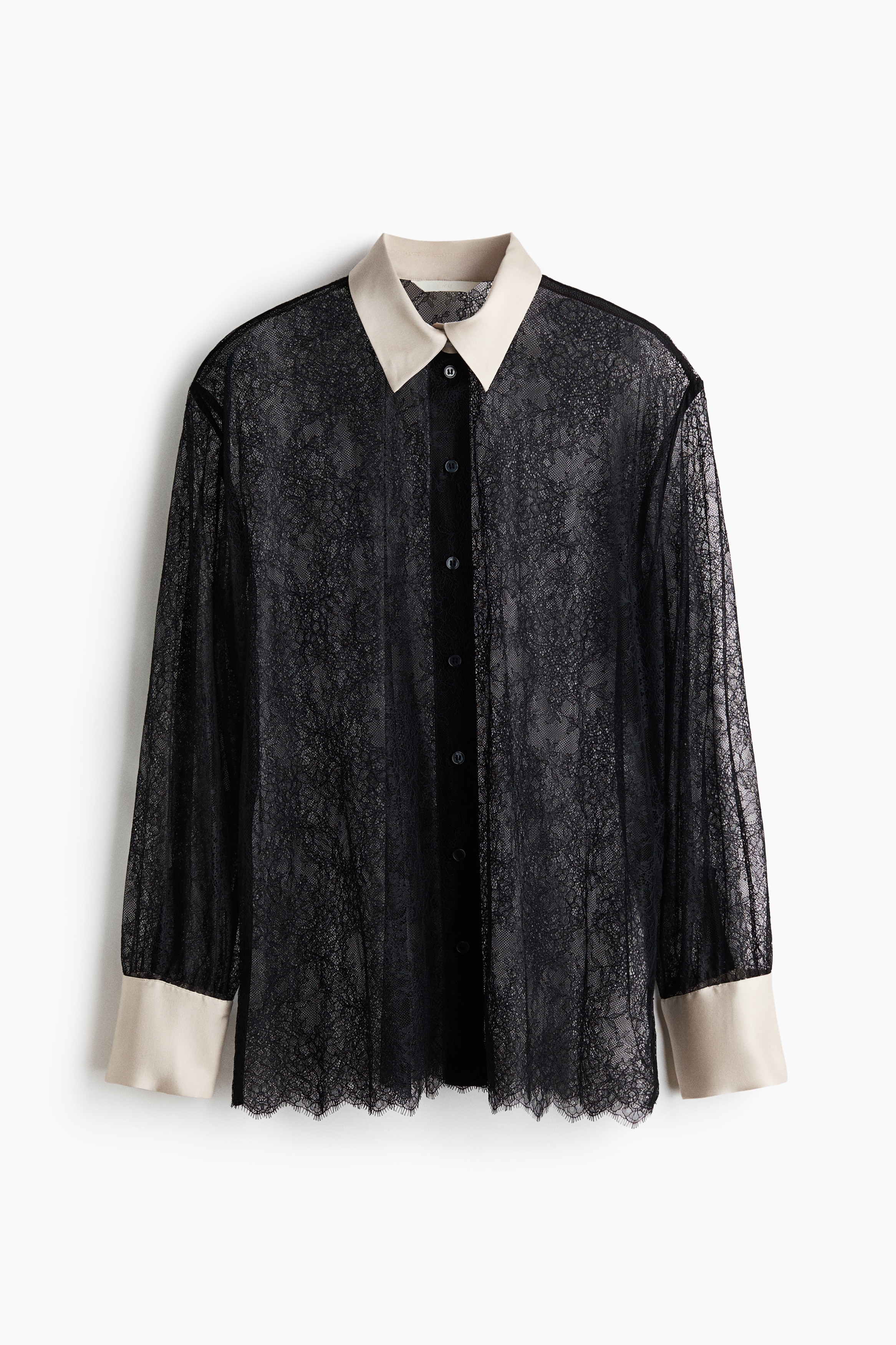 An oversized shirt in black lace, featuring a contrasting cream-coloured collar and cuffs, is being worn by the model. The sheer shirt is layered over a black bralette and styled with black trousers.