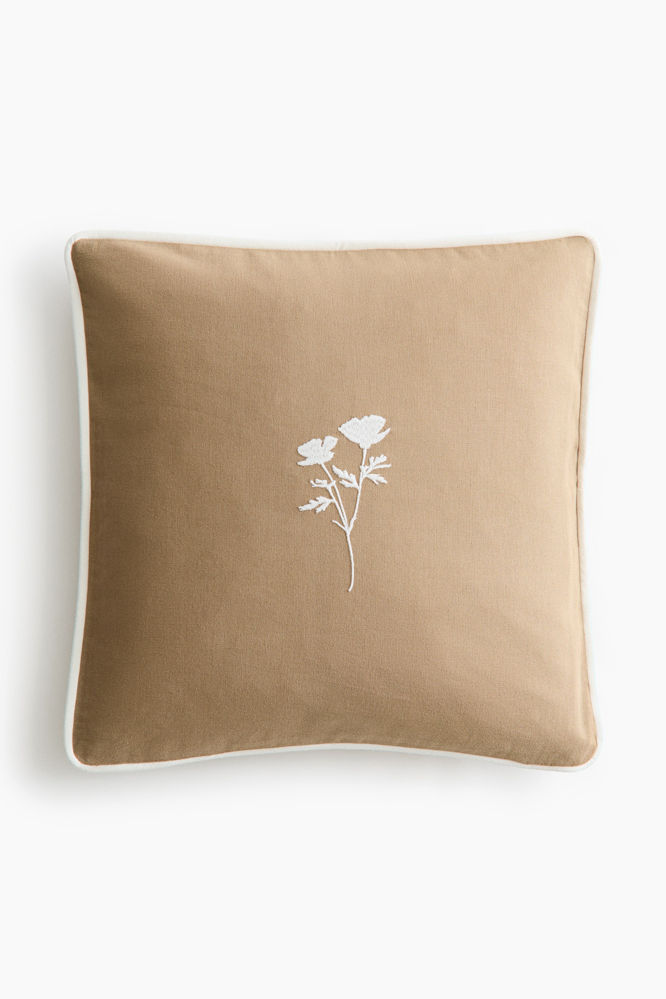 View larger image: The front of a square tan cushion cover crafted from cotton canvas is displayed. At its center, a white embroidered floral motif elegantly stands out, while contrasting white piping outlines its edges.