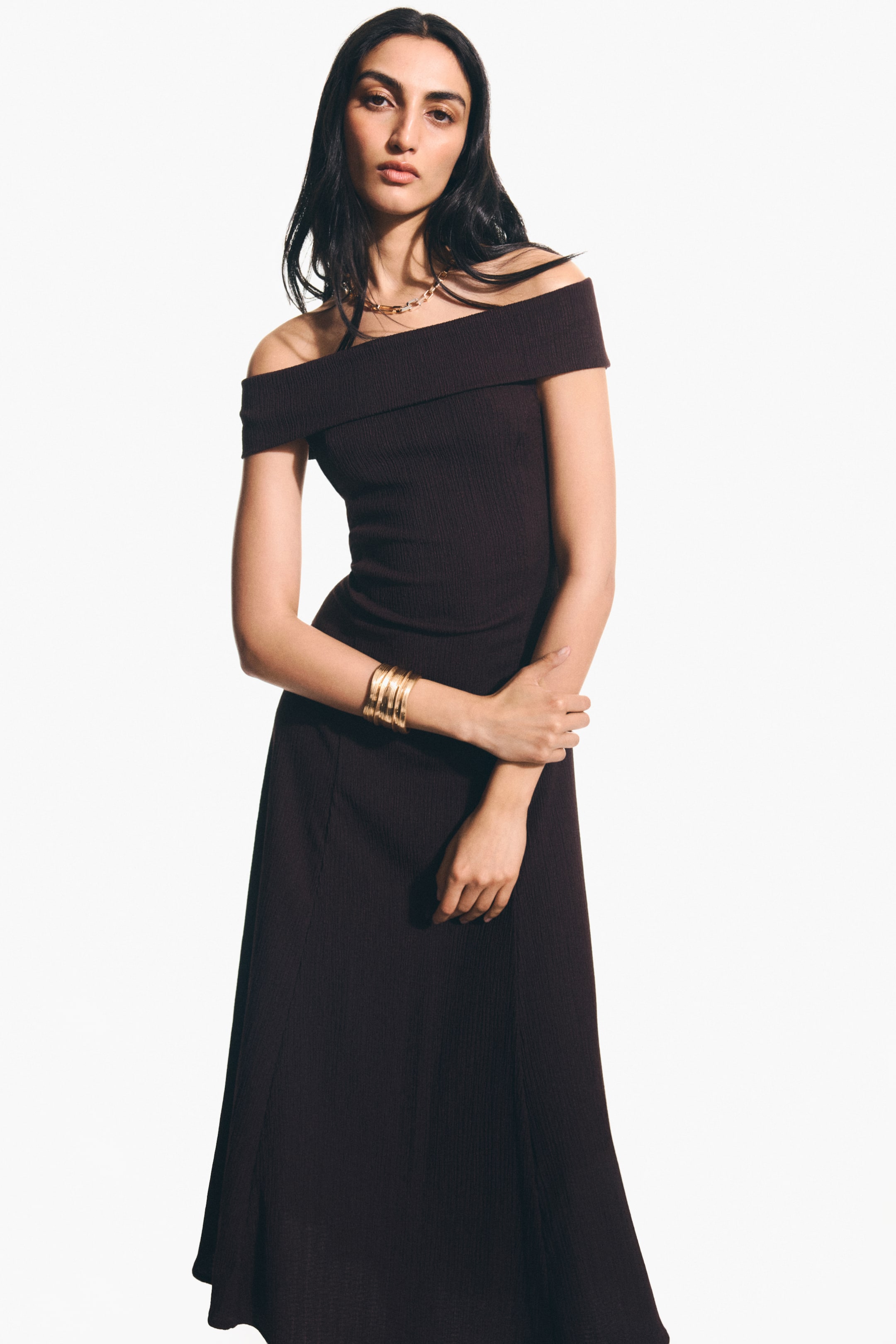 View larger image: A deep brown ribbed knit dress featuring an off-the-shoulder neckline with a folded band. The dress is crafted with a fitted bodice and an A-line skirt, extending to ankle length.