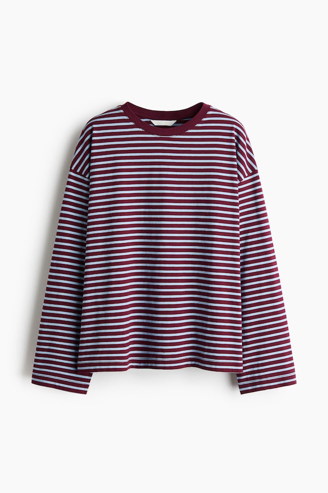 Una camiseta de algodón de manga larga aparece colgada en vista frontal, mostrando rayas horizontales en burdeos y azul claro. La prenda presenta un escote redondo liso en burdeos, hombros caÃdos y un bajo de corte recto. - 1